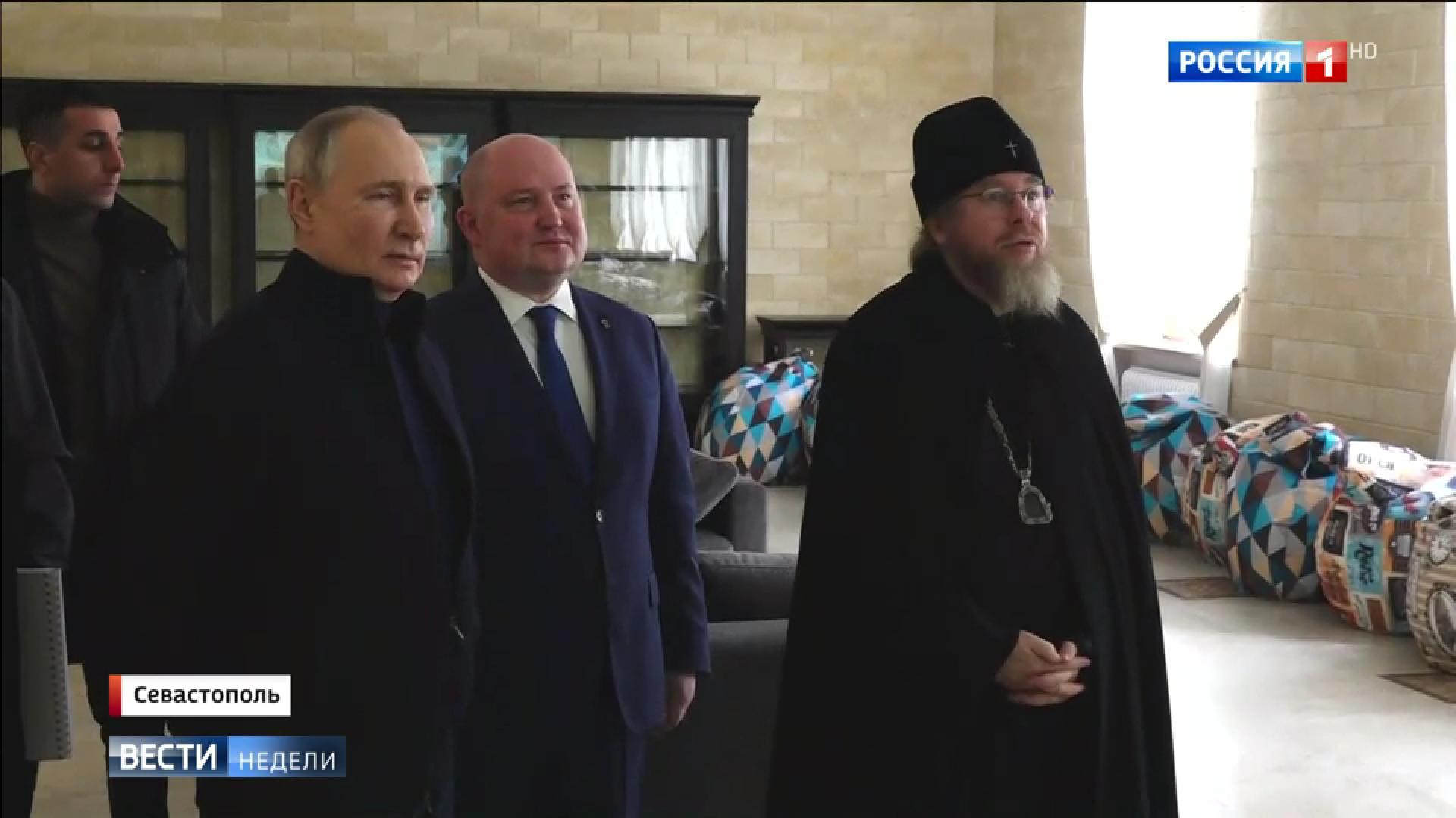 Putin w sportowym stroju w towarzystwie urzędnika w garniturze i popa w sutannie
