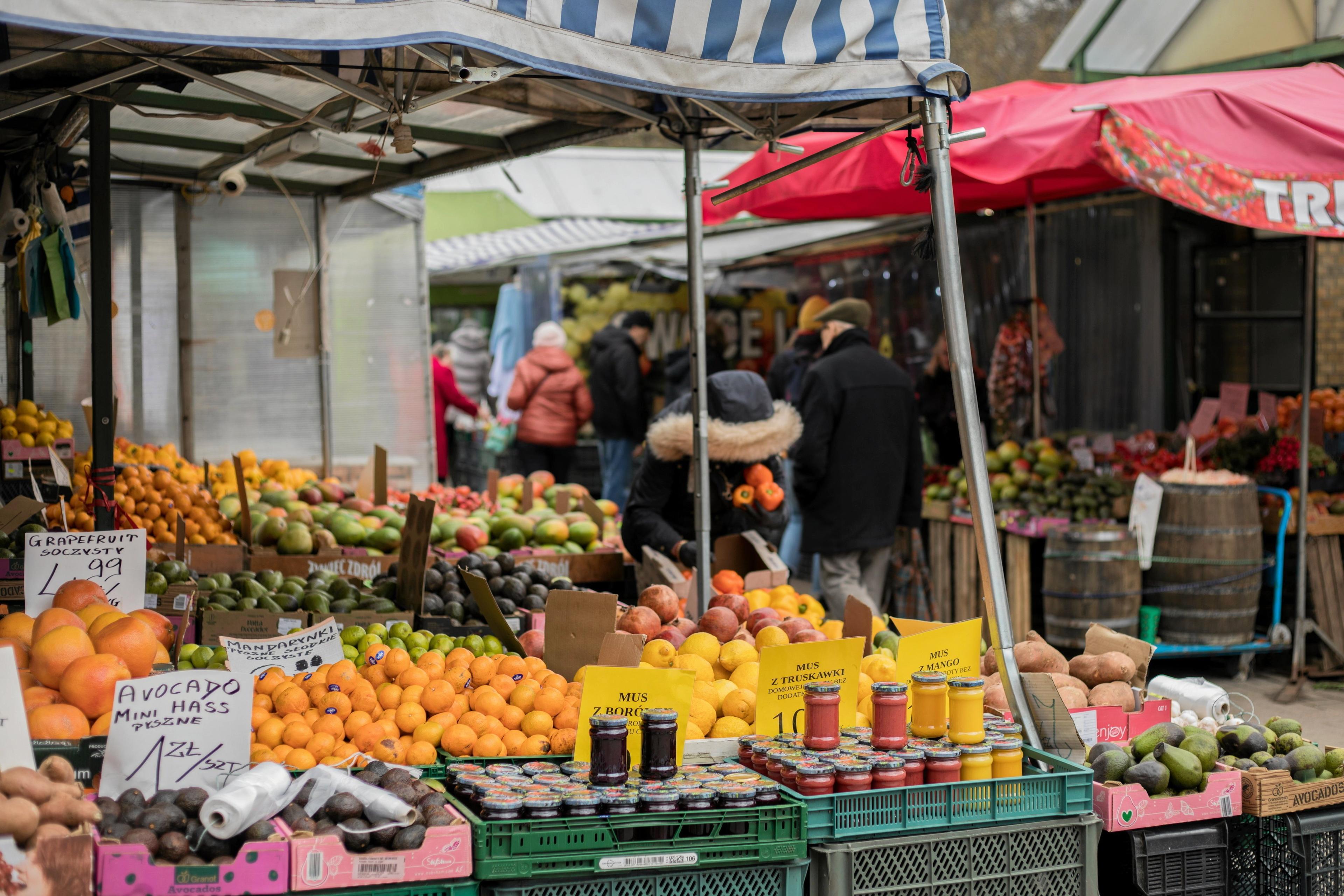 Kobieta pochylona nad owocami i przetworami na bazarze, patrzy na ceny