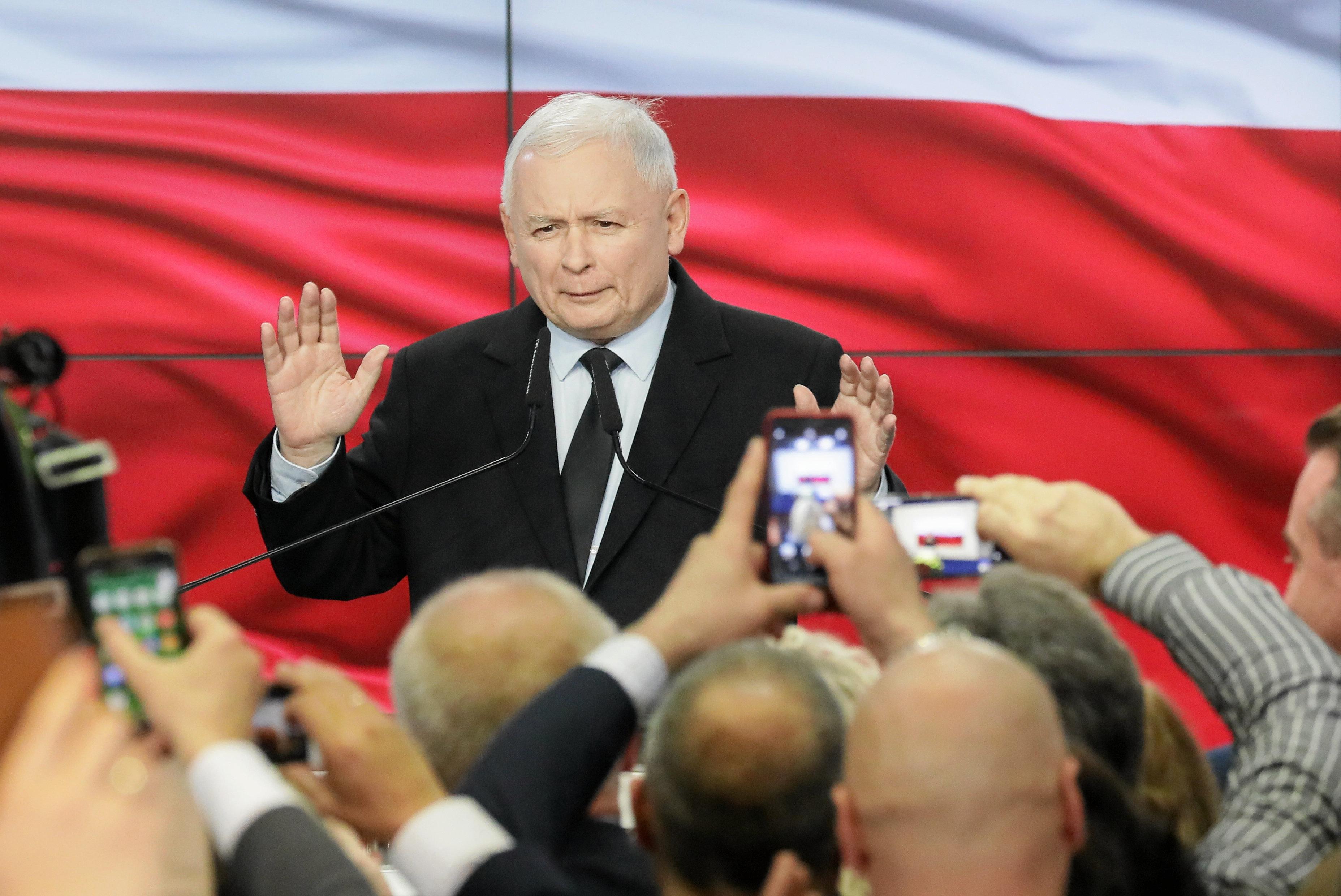 Jarosław Kaczyński przed tłumem zwolenników podczas wieczory wyborczego. Za nim na ekranie wyświetlana jest flaga Polski