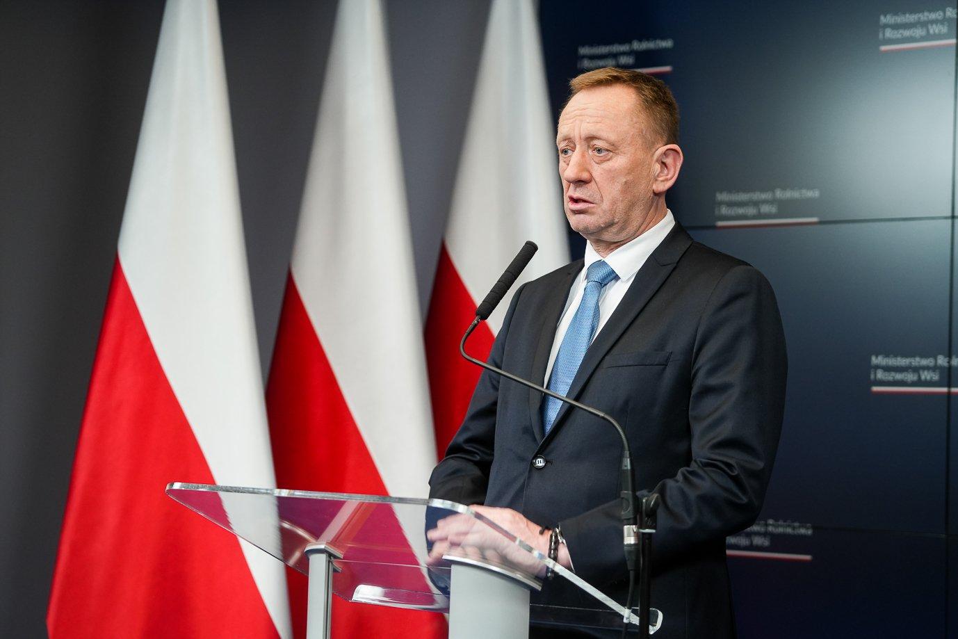 Męzczyzna przy mównicy na tle polskich flag (min. Telus)