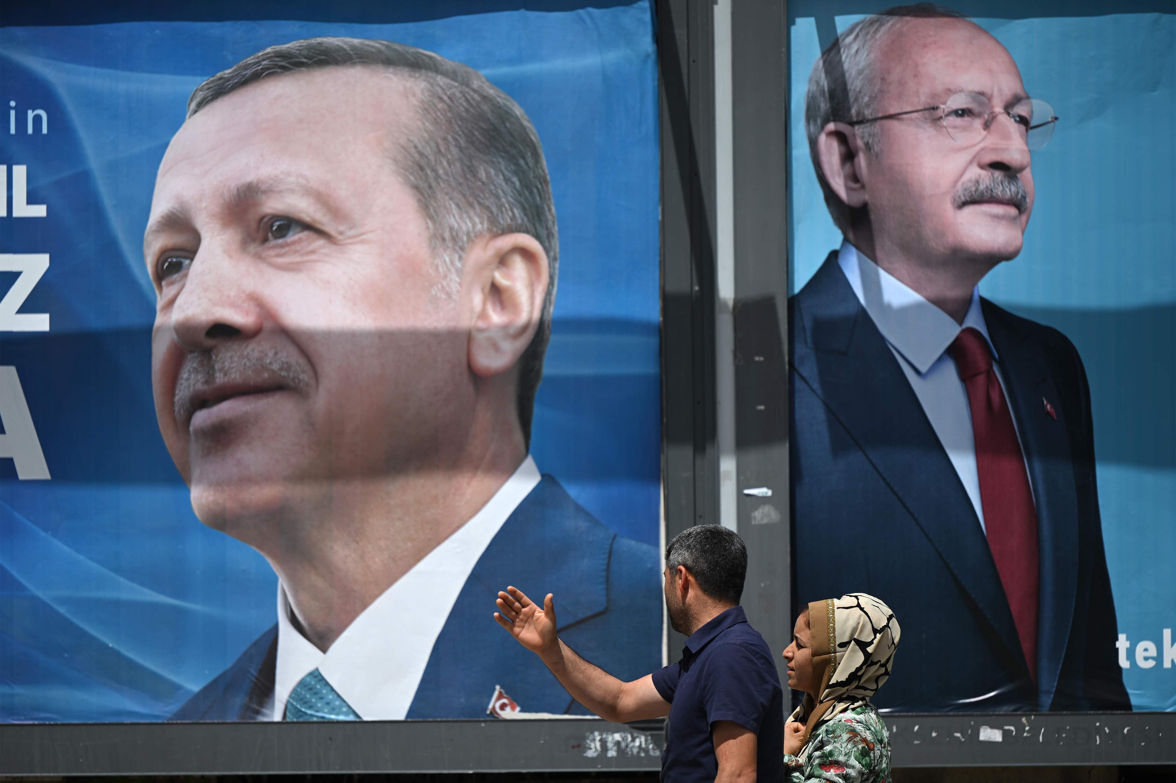 Plakaty kandydatów w wyborach w Turcji, na ich tle przechodzą przechodnie.