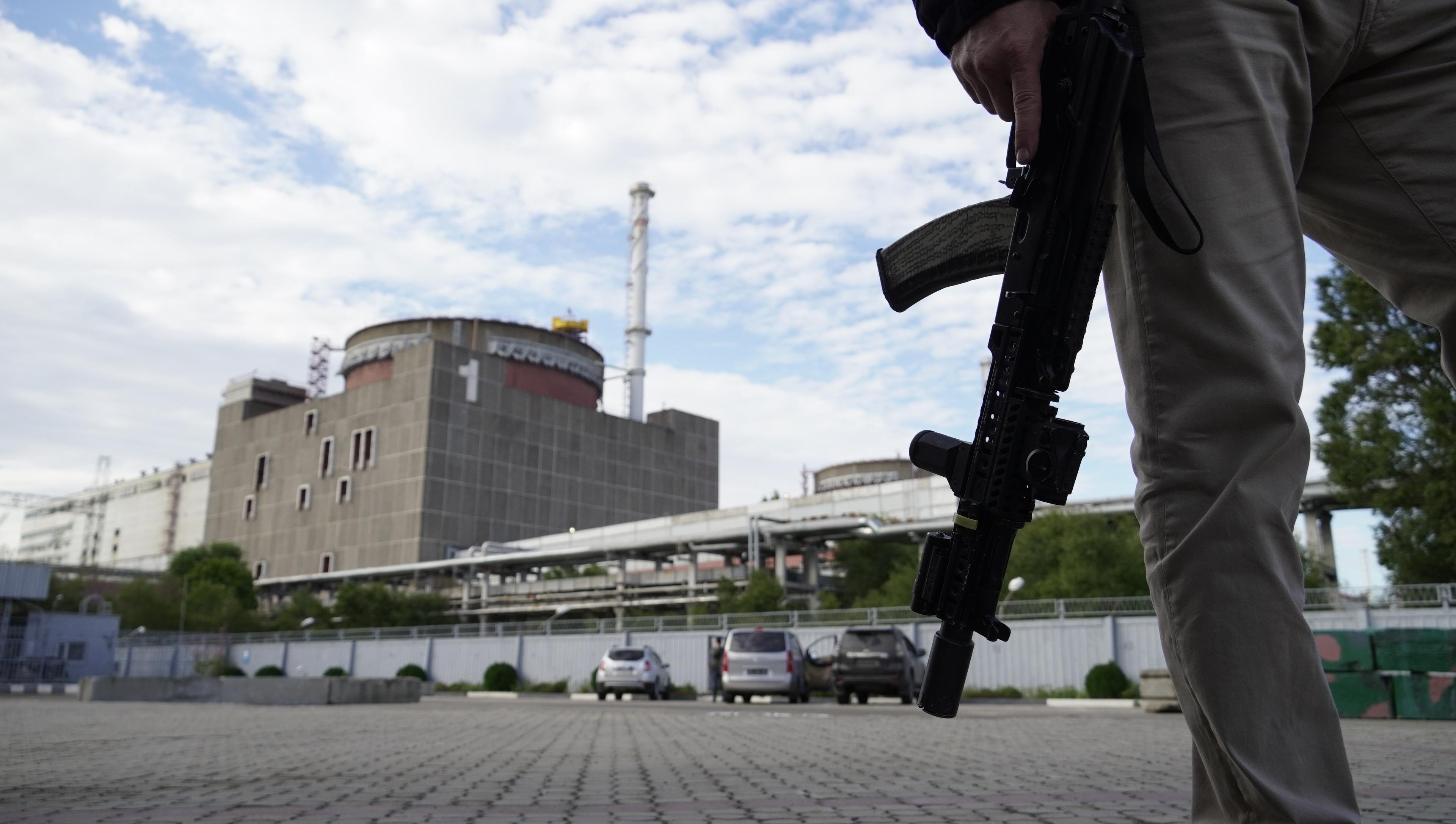 Wojskowy z karabinem patrzy na wielki budynek - Zaporoską Elektrownię Atomową
