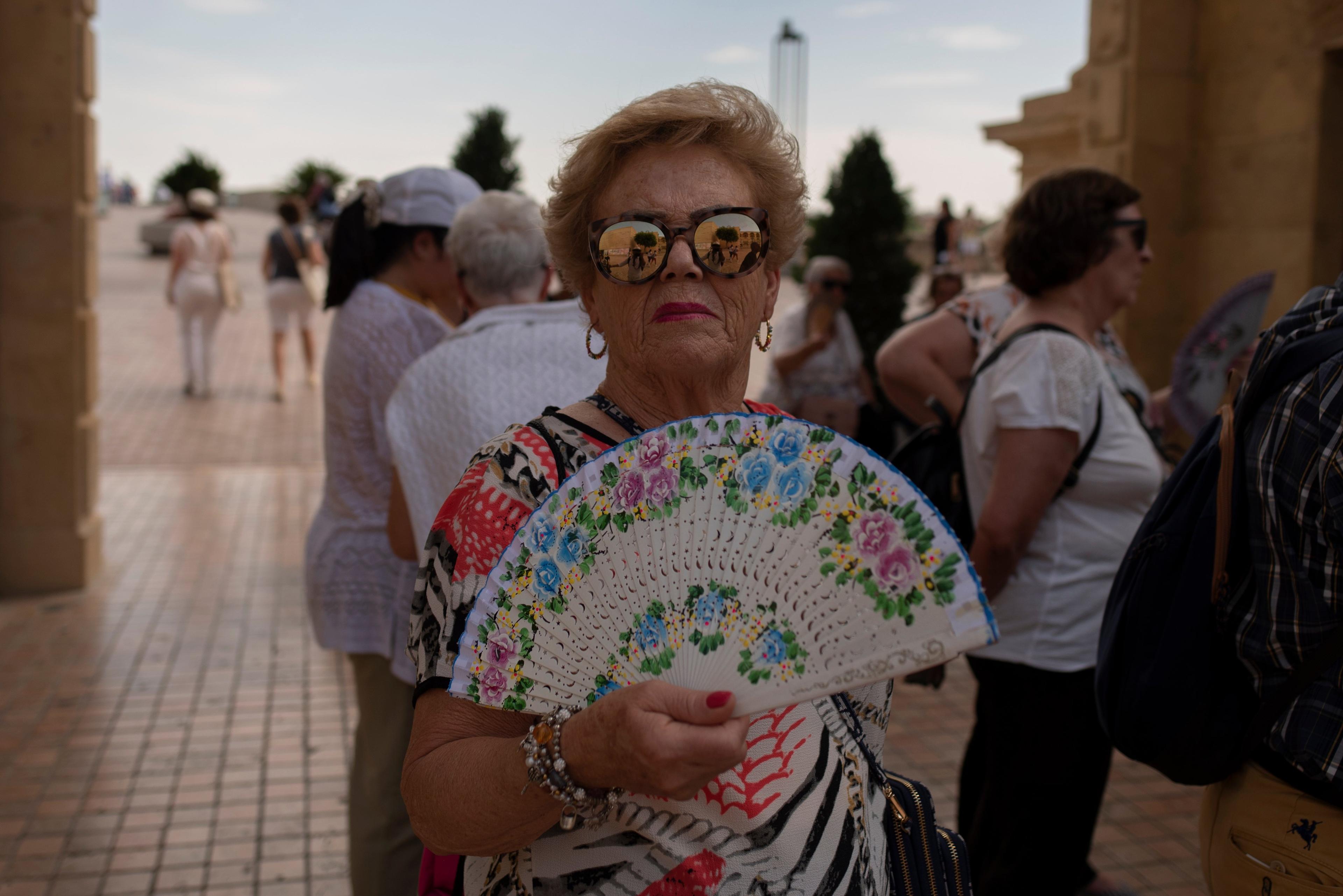 starsza pani w przeciwsłonecznych okularach i z wachlarzem na tle tłumu
