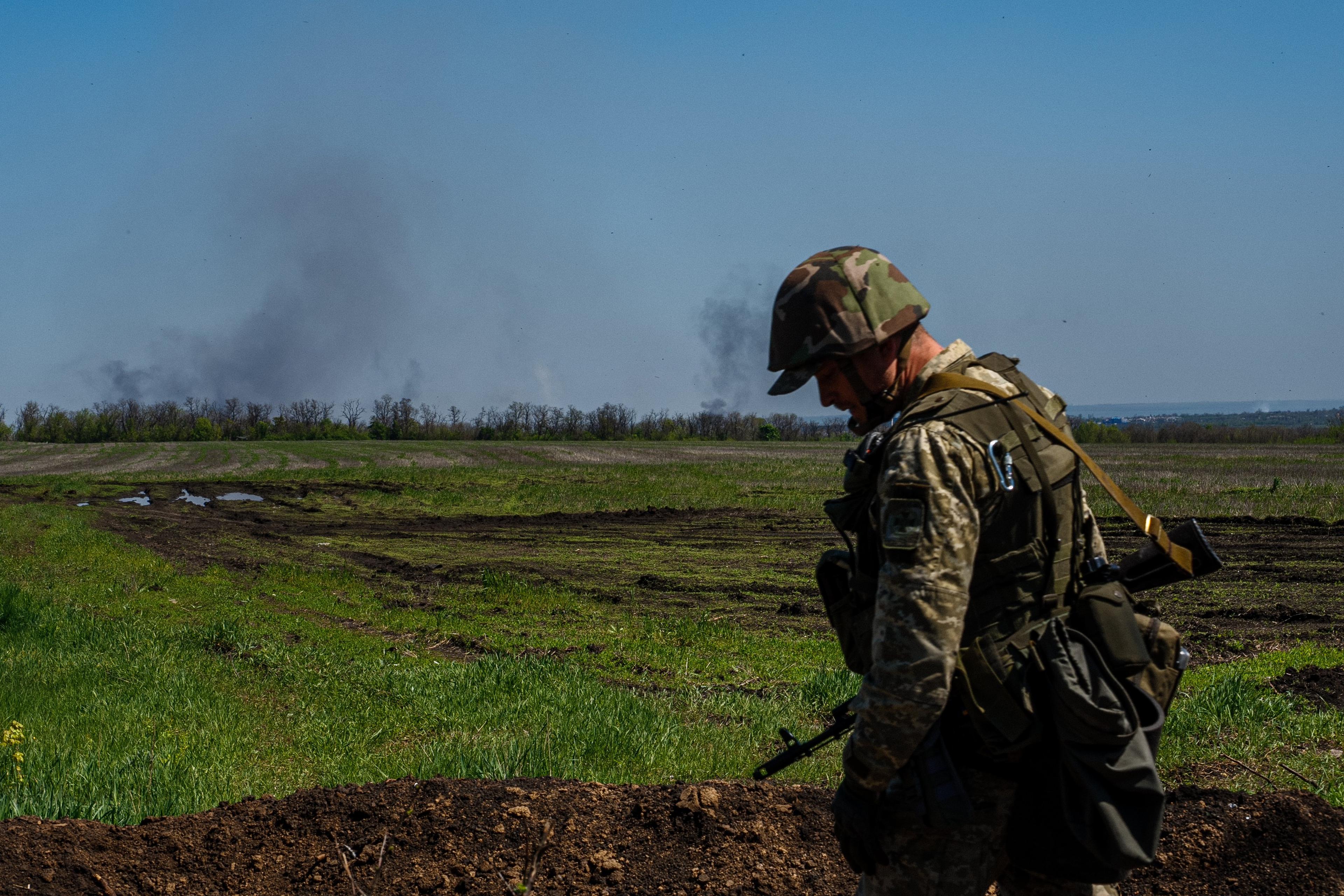 ukraiński żołnierz, w tle zielone pole a dale unoszący sie dym