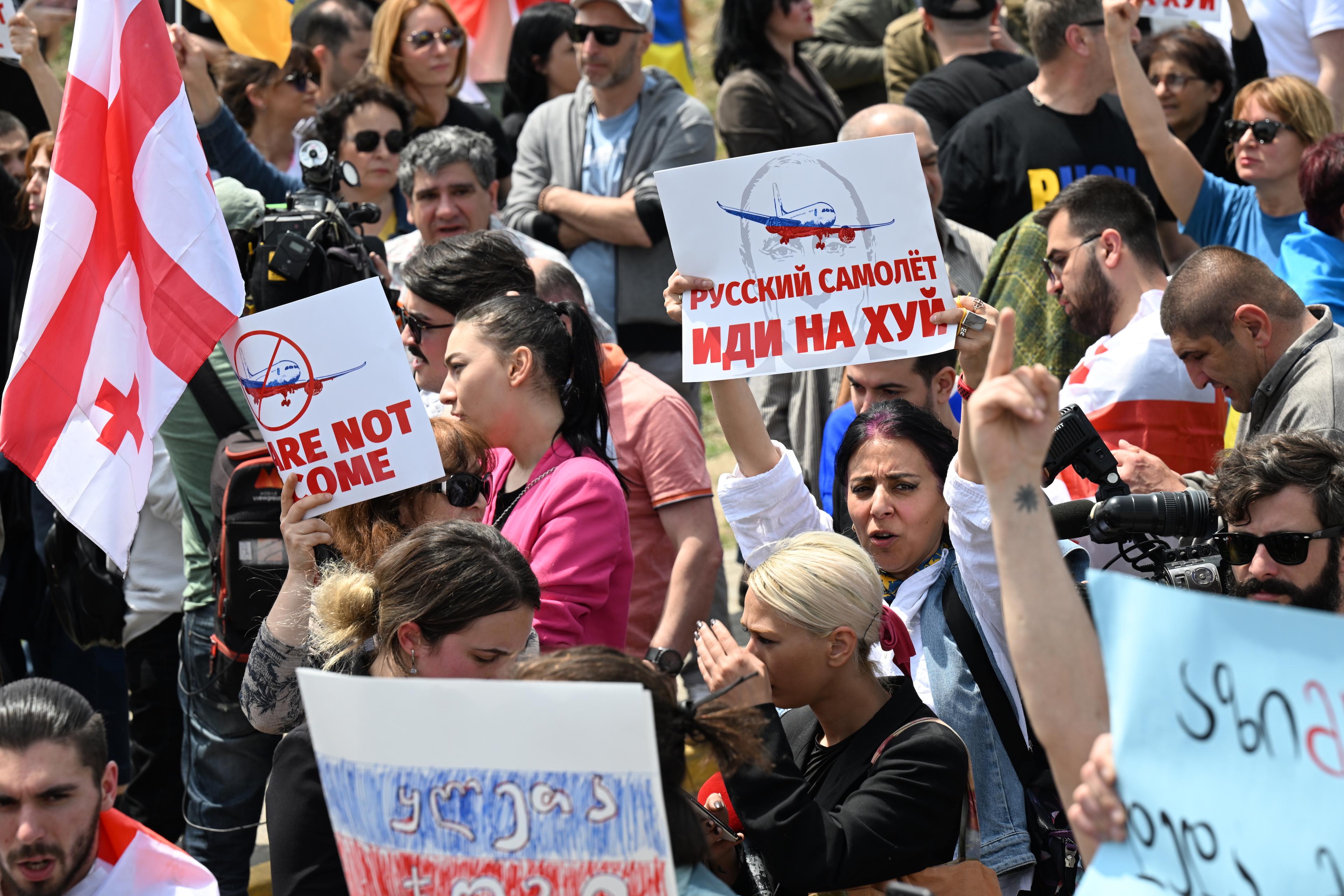 protestujący Gruzini trzymają flagi Gruzji transparent z napisem cyrylicą: Russkij samoliot idi na chuj