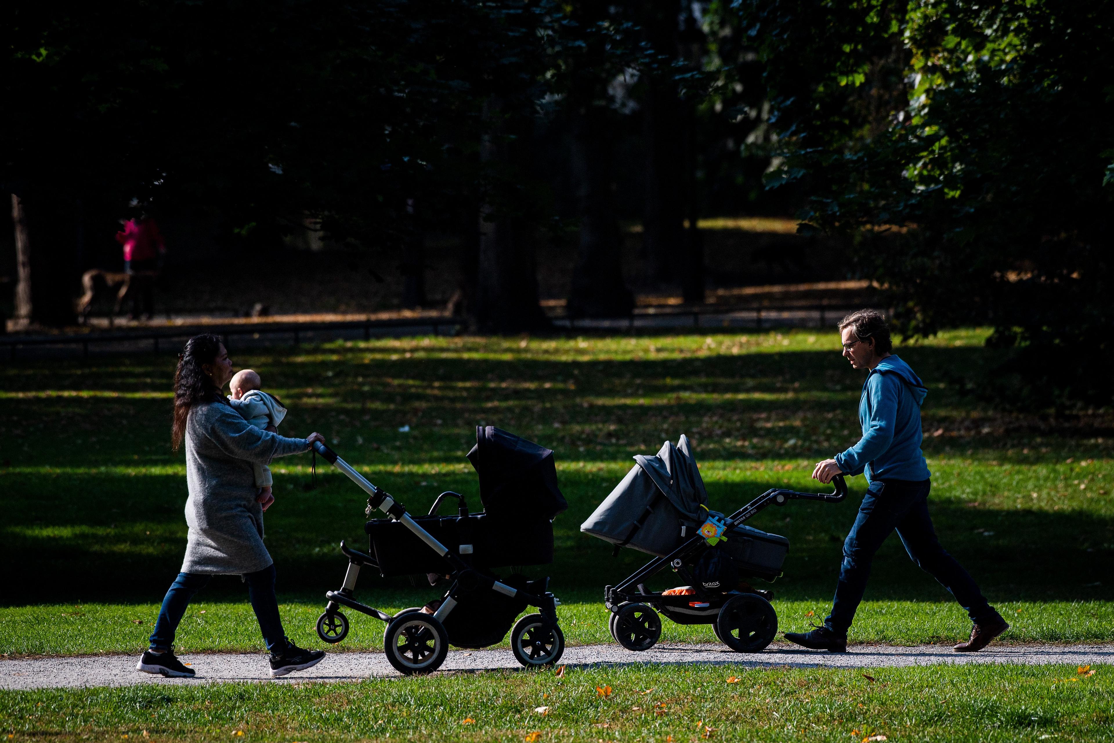 Kobieta i mężczyzna w parku w Sztokholmie, mijają się z naprzeciwka, prowadząc dziecięce wózki