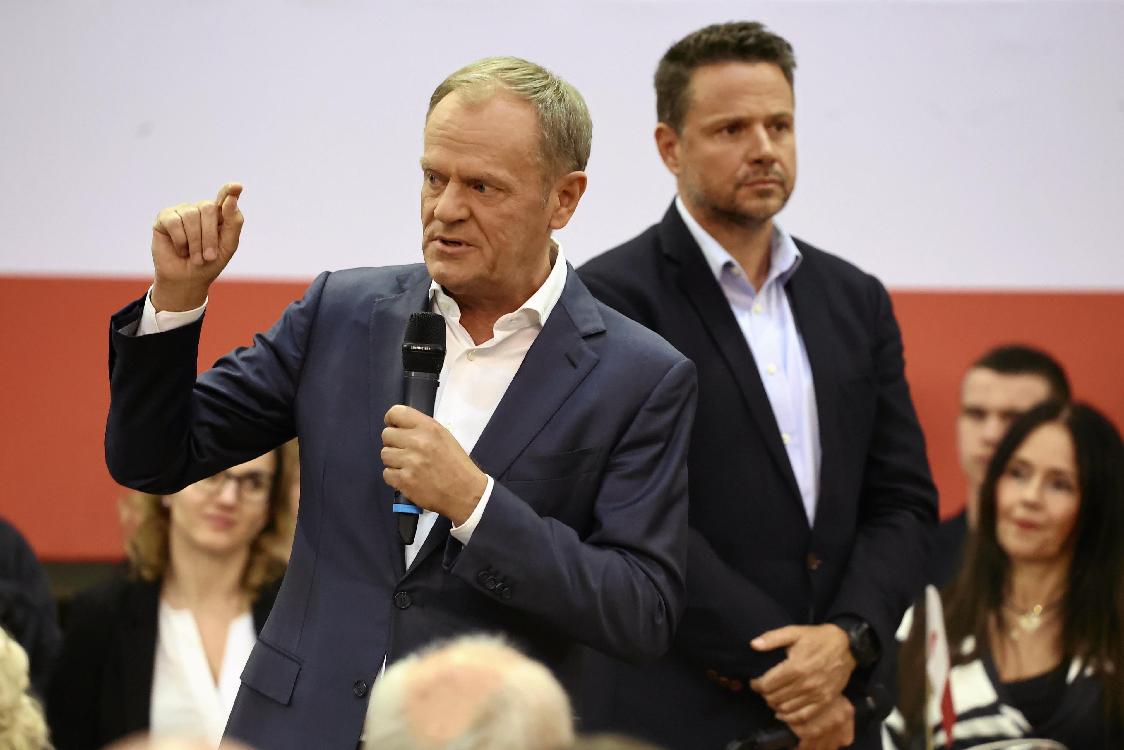 Dwaj mężczyźni w marynarkach bez krawatów: Donald Tusk mówi i gestykuluje, Rafał Trzaskowski słucha