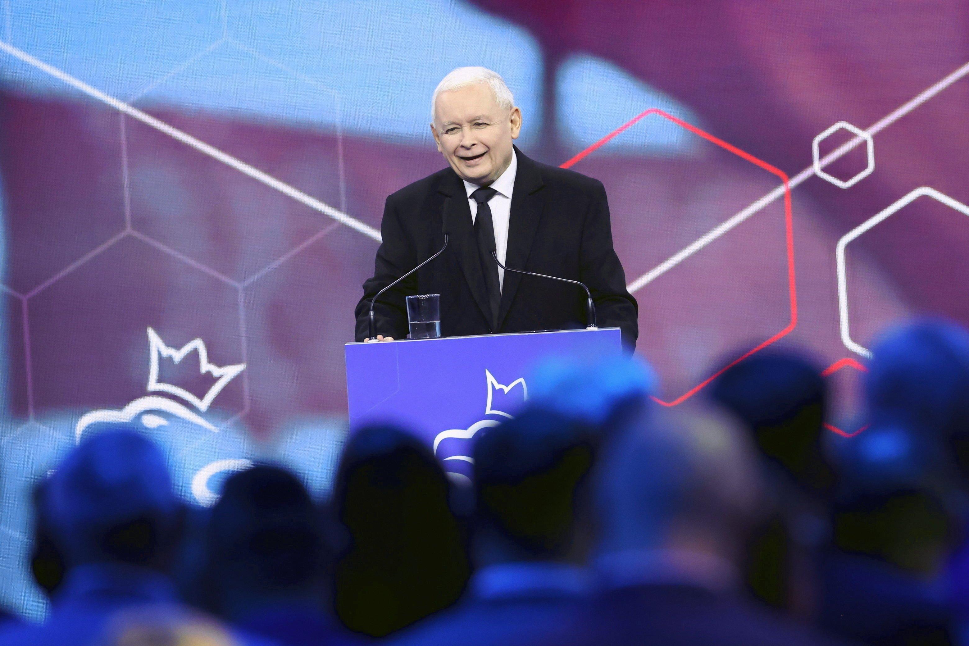 Mężczyzna, Jarosąłw Kaczyński, przemawia na tle geometrycznych figur