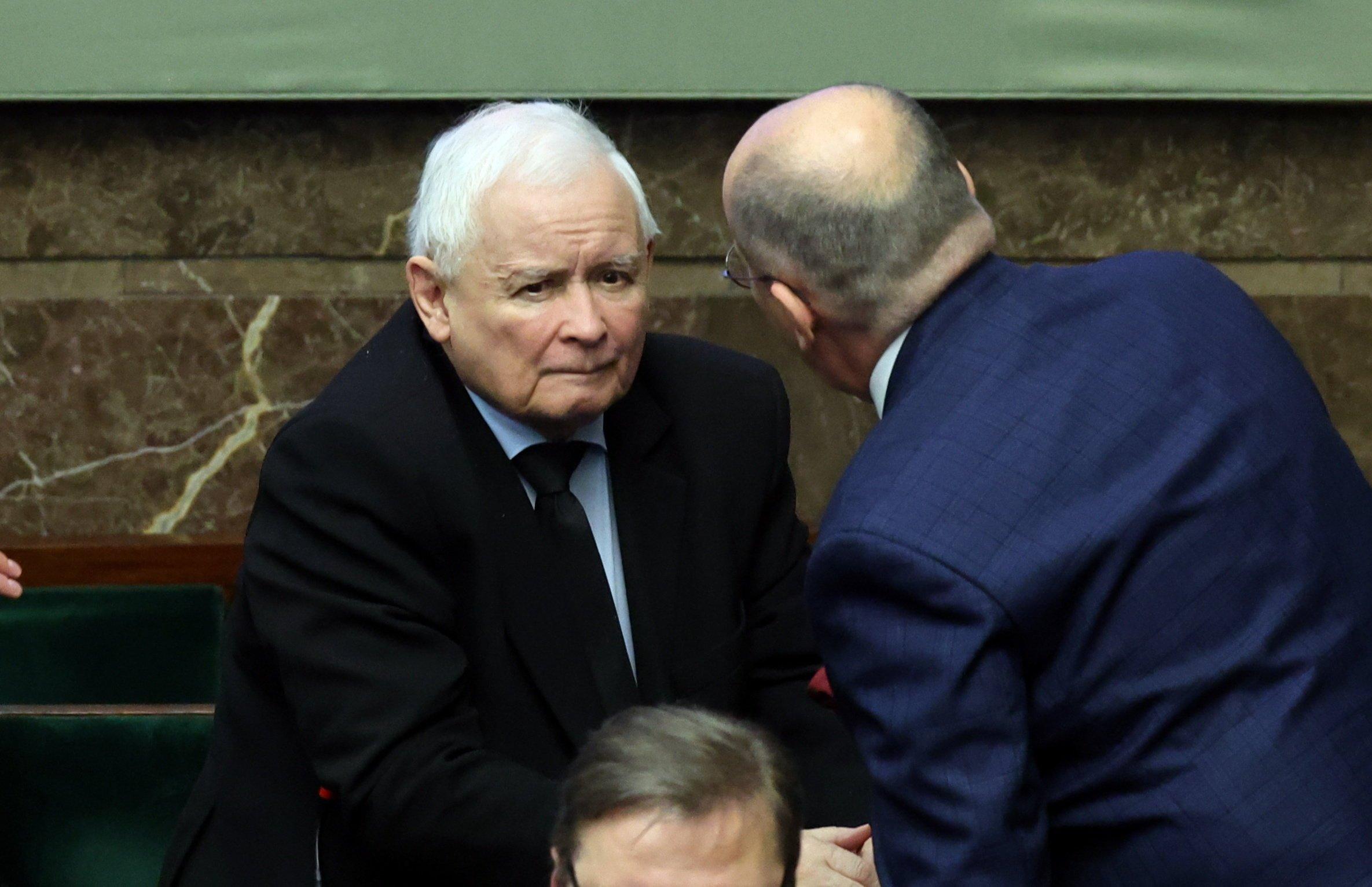 Prezes PiS Jarosław Kaczyński siedzie w ławach rządowych w Sejmie. Pochyla się nad nim jakiś mężczyzna