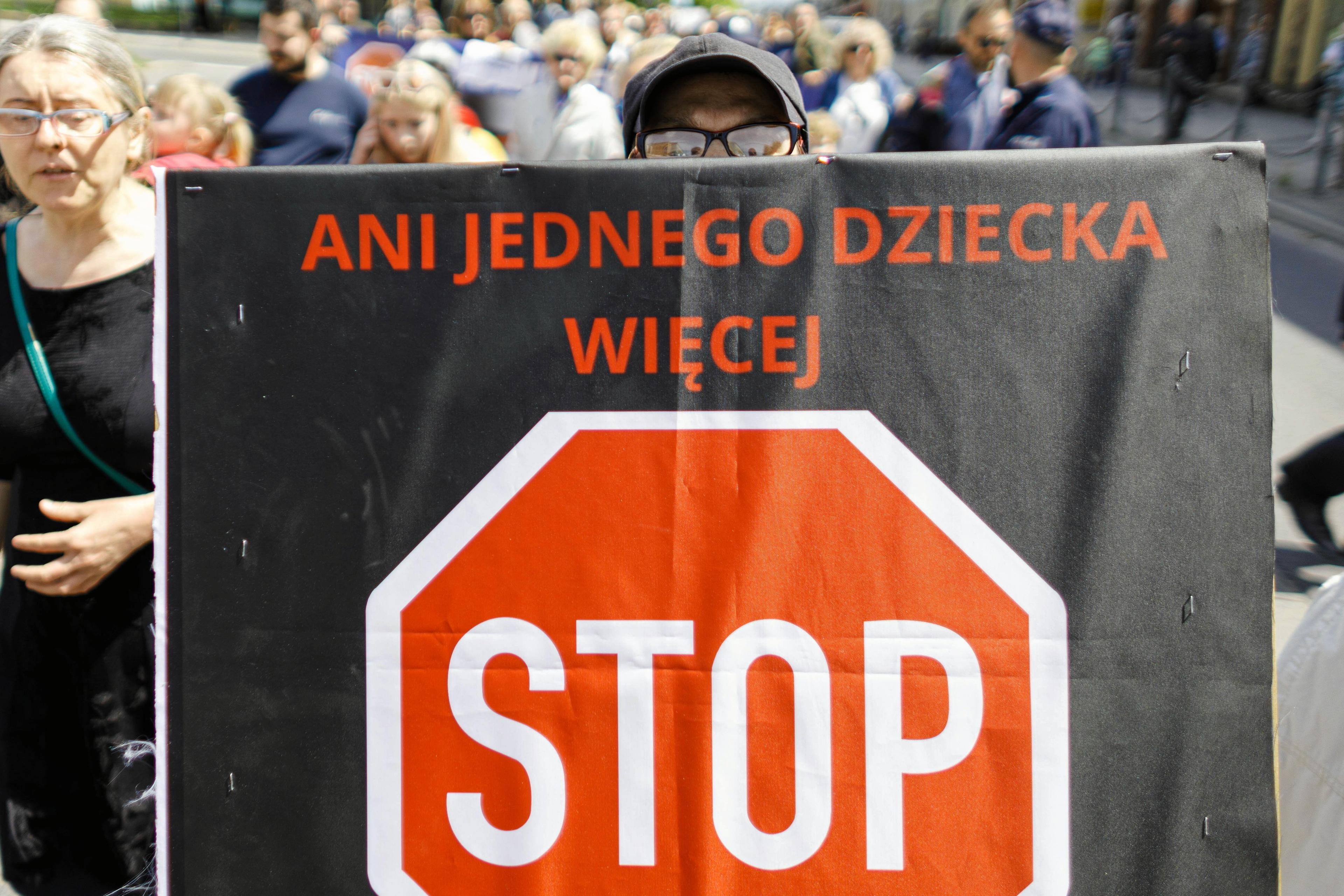 Mężczyzna trzyma plakat przeciw przemocy w rodzinie. Napis: "Ani jednego dziecka więcej. STOP"