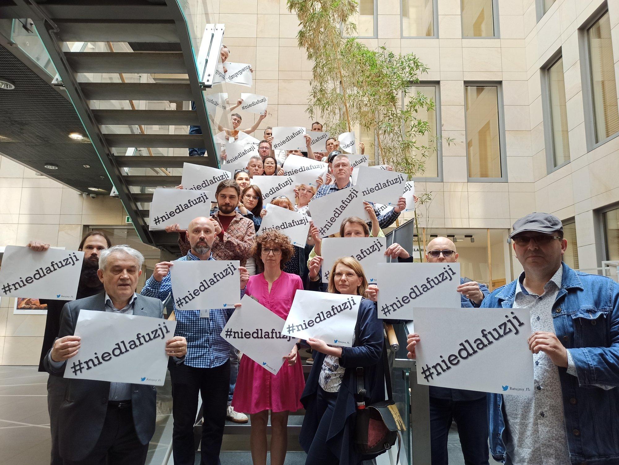 Kilkanascie osób trzyma w rękach kartki z napisem #nie dla fuzji