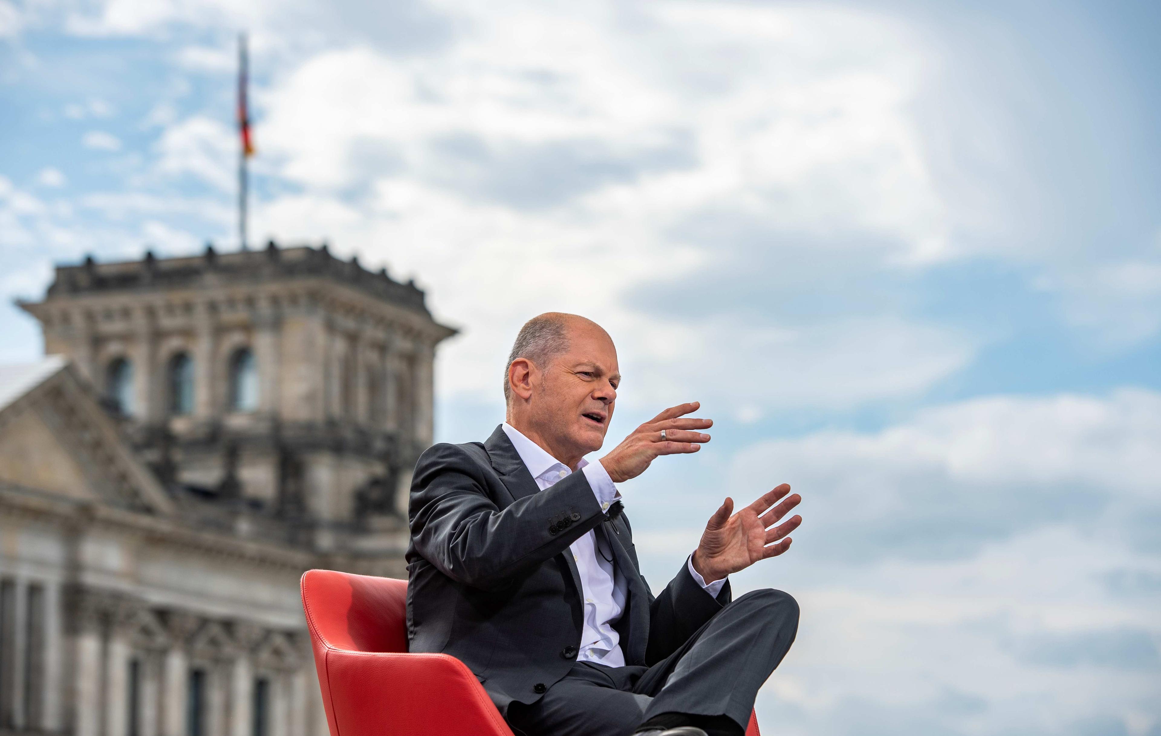 Kandydat na kanclerza Niemiec Olaf Scholz udziela wywiadu, siedząc na czerwonym fotelu na tle budynku Reichstagu, siedziby Bundestagu w Berlinie. Koalicja wyborcza w Niemczech.