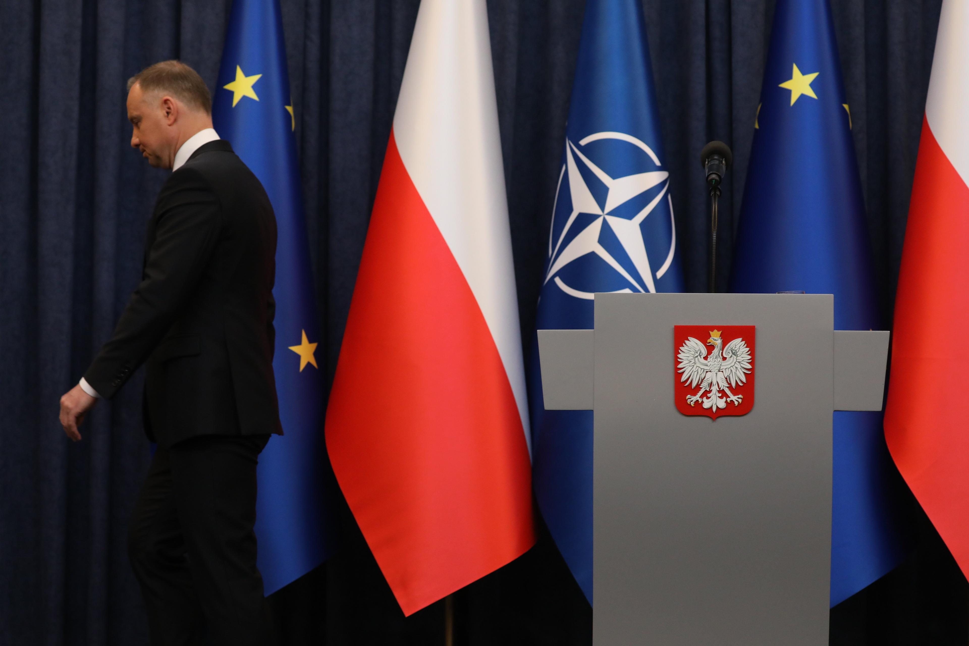 Andrzej Duda schodzi z podestu w sali konferencyjnej w Pałacu Prezydenckim, jest odwrócony plecami do mównicy, w tle flagi Polski, UE i NATO