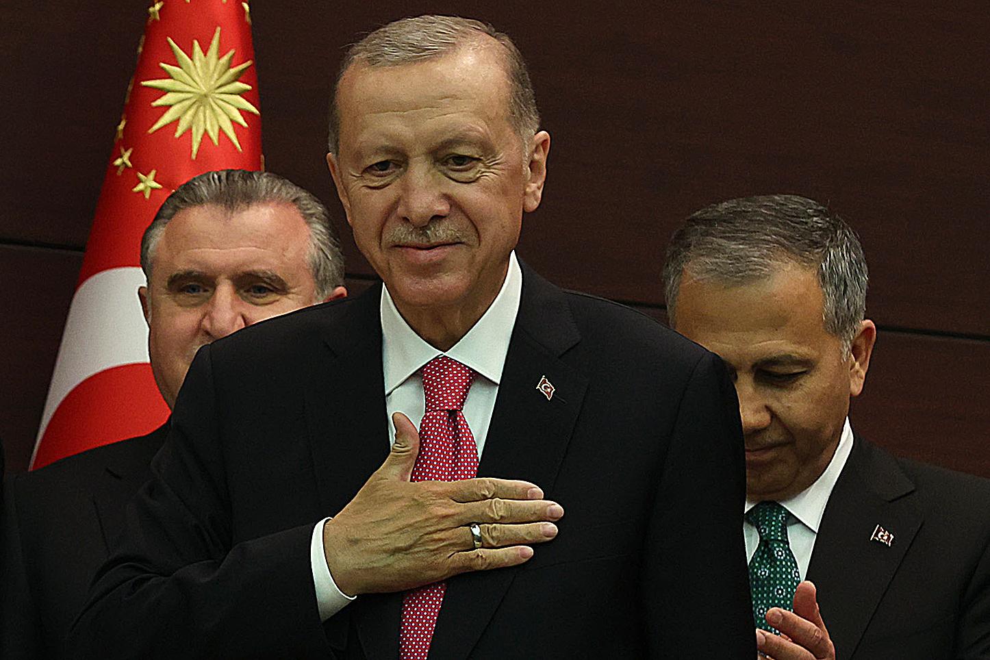 Mężczyzna w garniturze (prezydent Erdogan) kładzie rękę na piersi