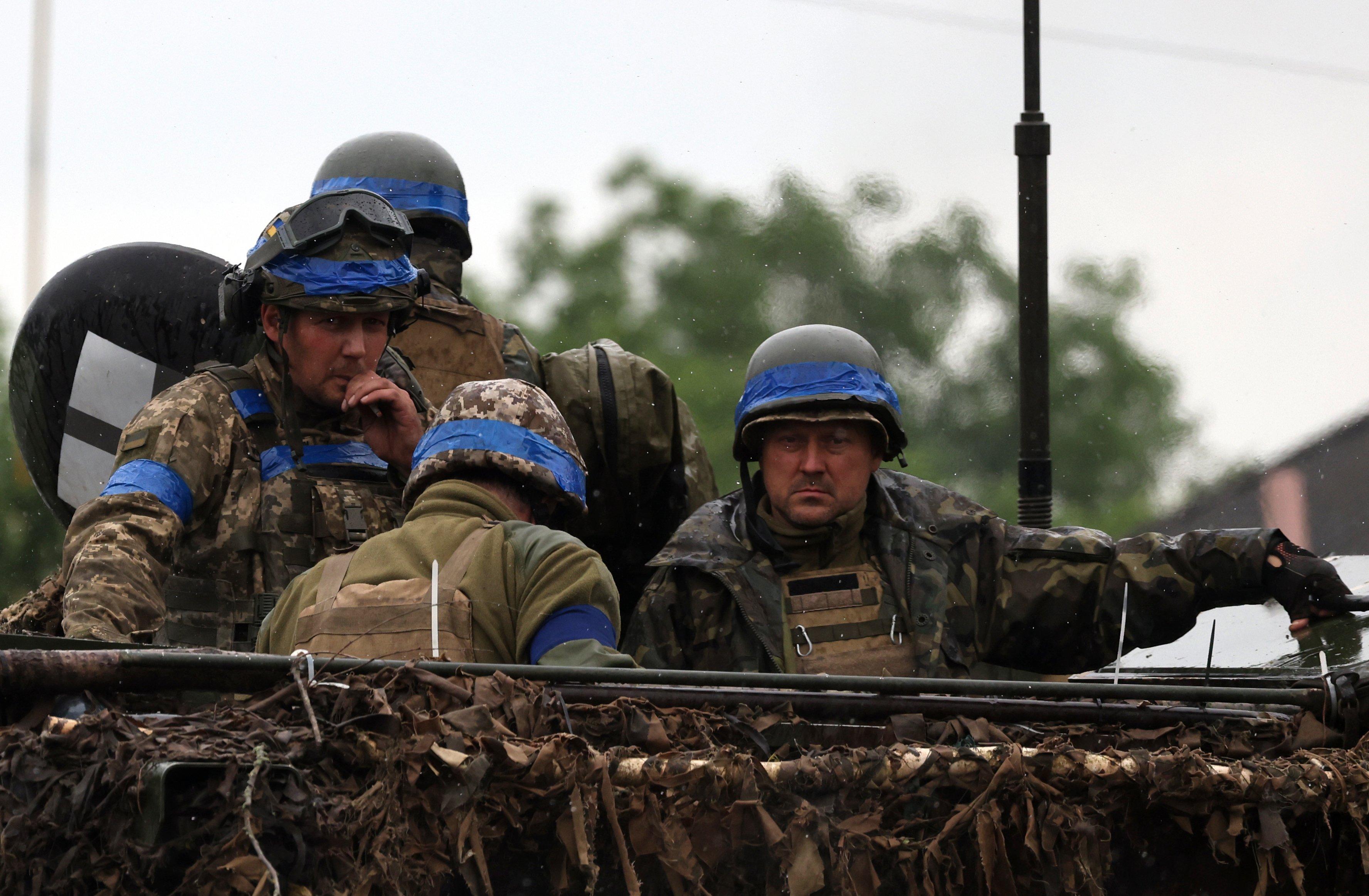 Mężczyźni na wozie opancerzonym, w mundurach frontowych i hełmach przepasanych niebieskim pasem