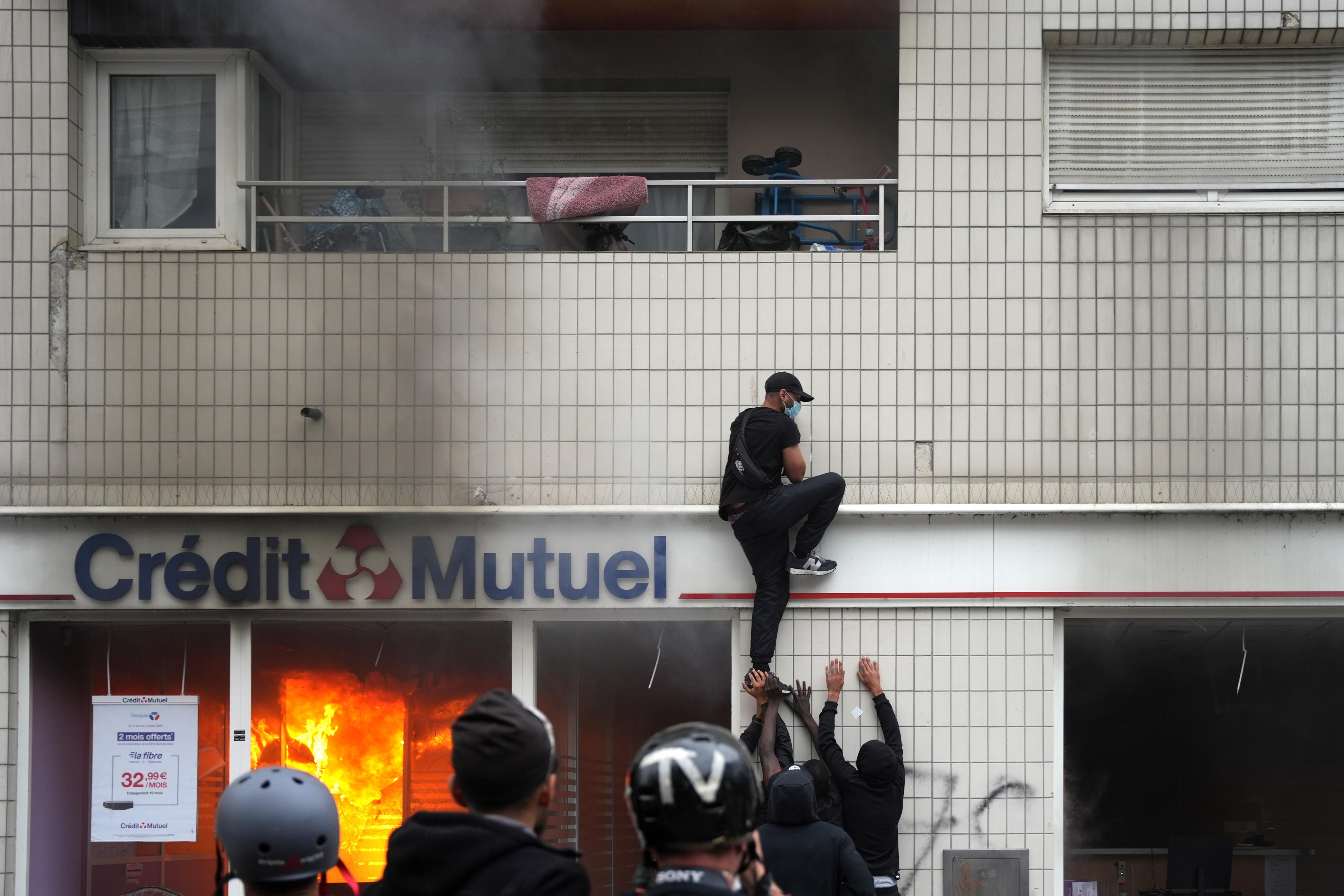 mężczyzna wspina się po ścianie budynku, za oknem widać płomienie