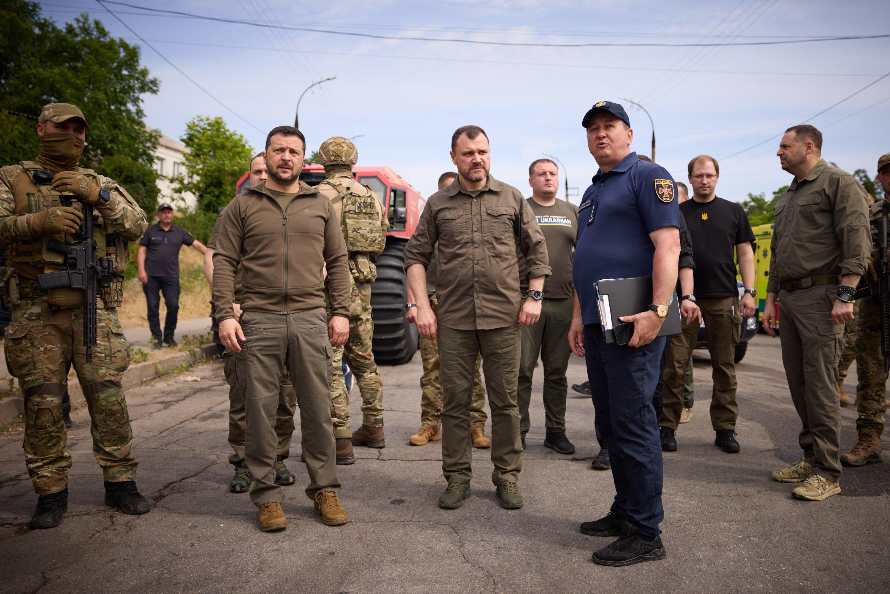 Męzczyźni w polowych mundurach, w tym prezydent Zełenski, patrzą przed siebie