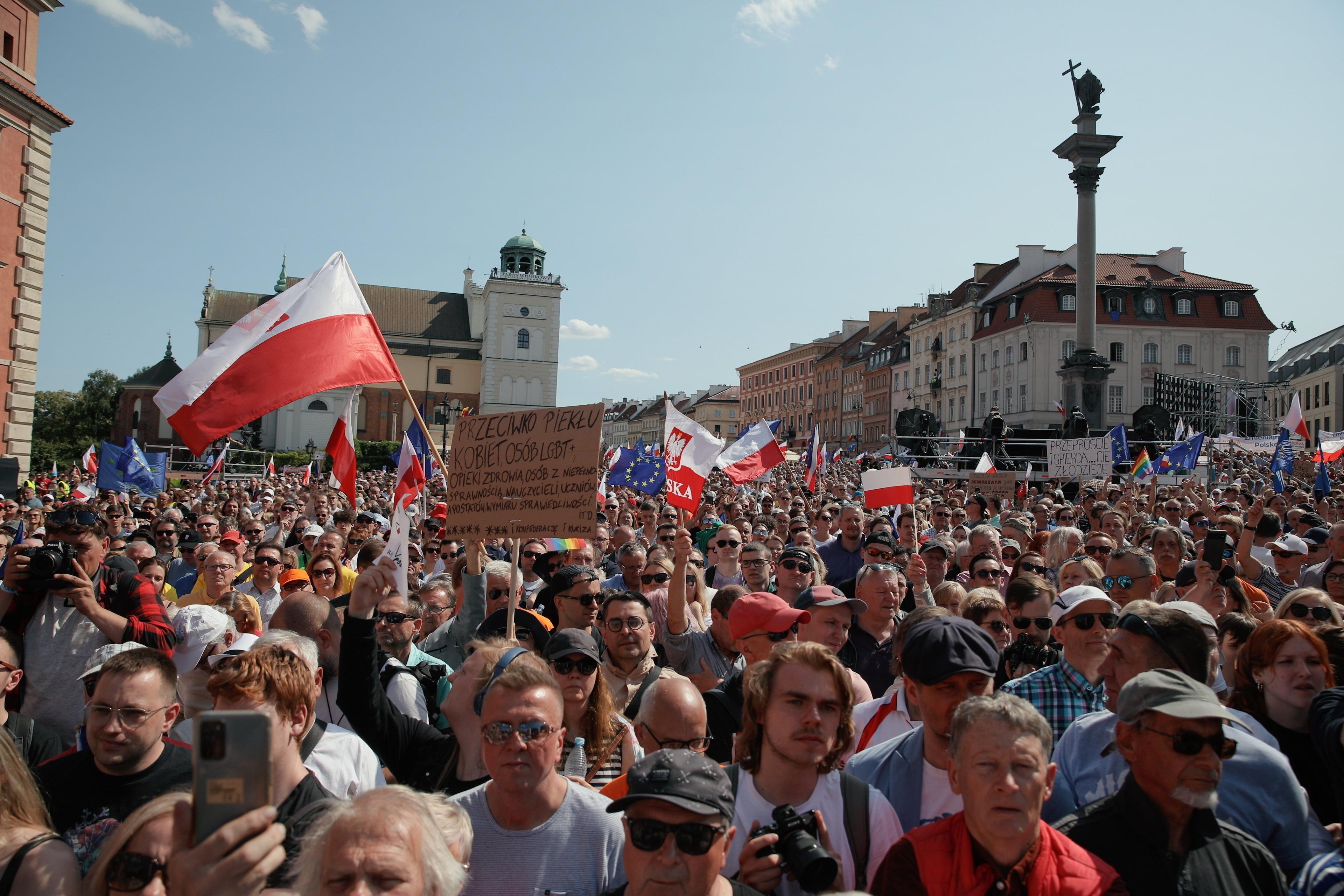 Tłum ludzi na placu Zamkowym (widać Kolumne Zygmunta). Mają biało-czerwone flagi