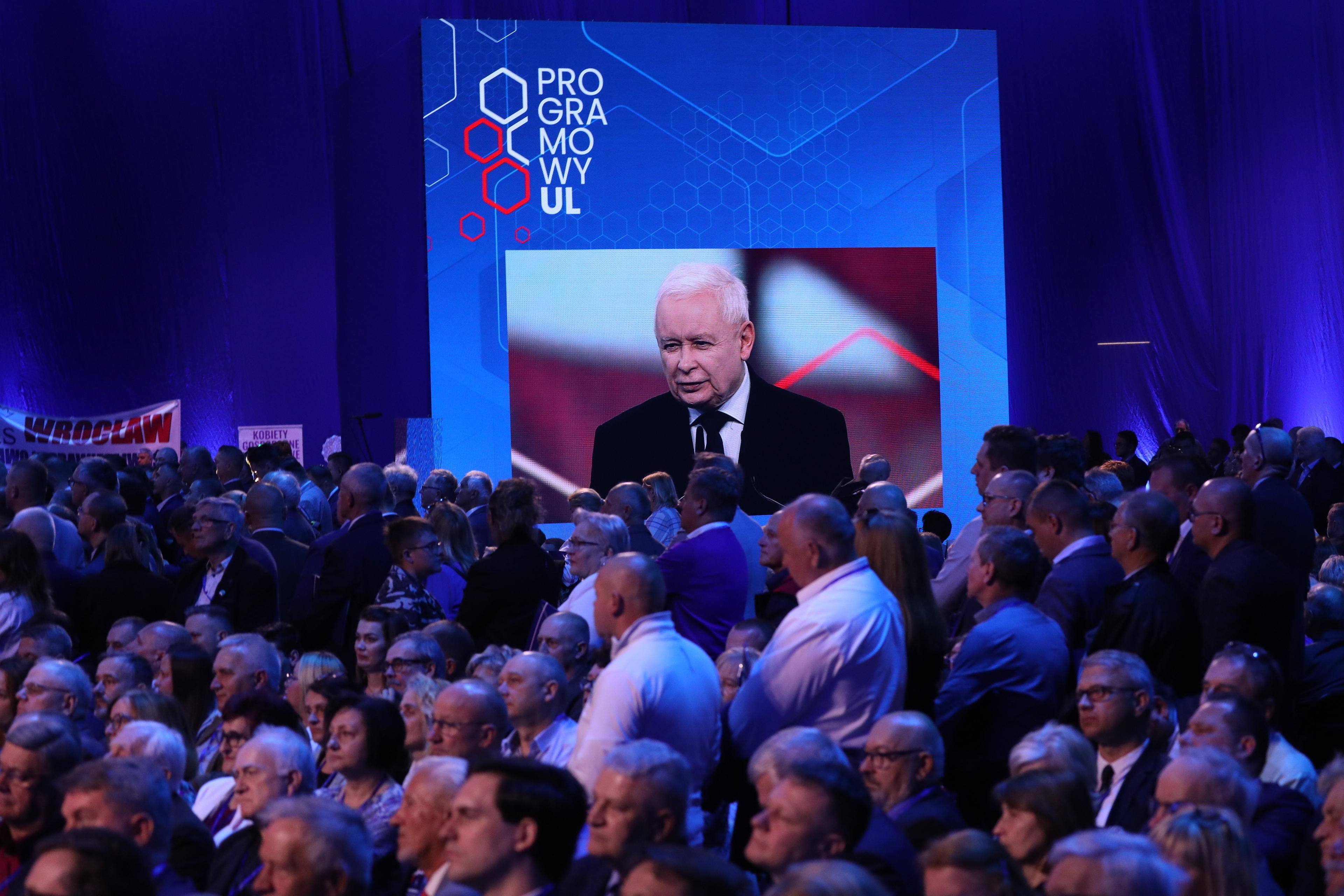 Na pierwszym planie publiczność siedzi na dużej sali, w tle na telebimie twarz Jarosława Kaczyńskiego, nad nim napis "Programowy Ul"