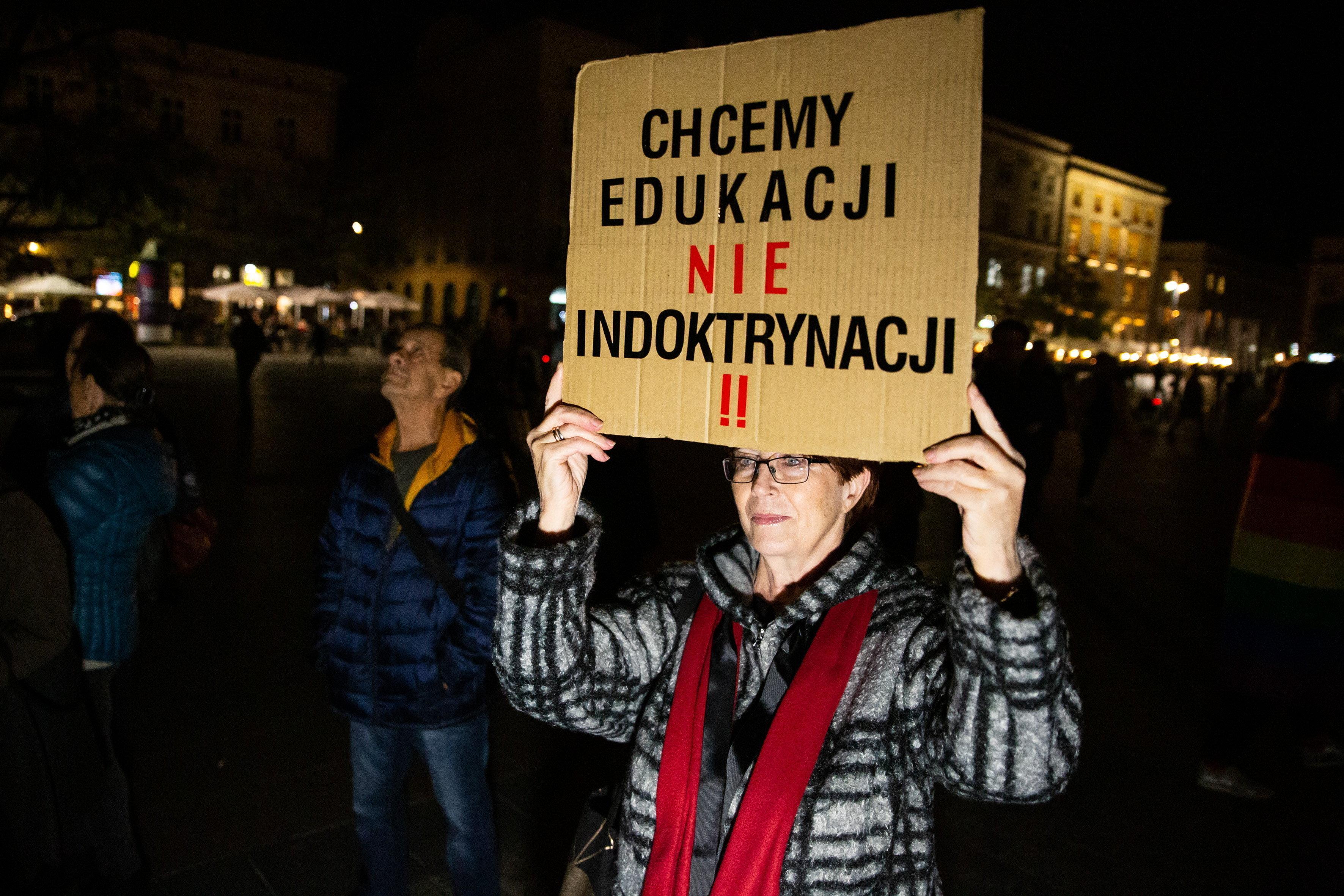 Na zdjęciu uczestniczka protestu przeciwko zmianom w prawie oświatowym. Kobieta w wieku średnim stoi z kartonem z hasłem "Chcemy edukacji nie indoktrynacji"