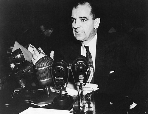 Mężczyzna w garniturze przemawia przed mikrofonami. Joseph McCarthy