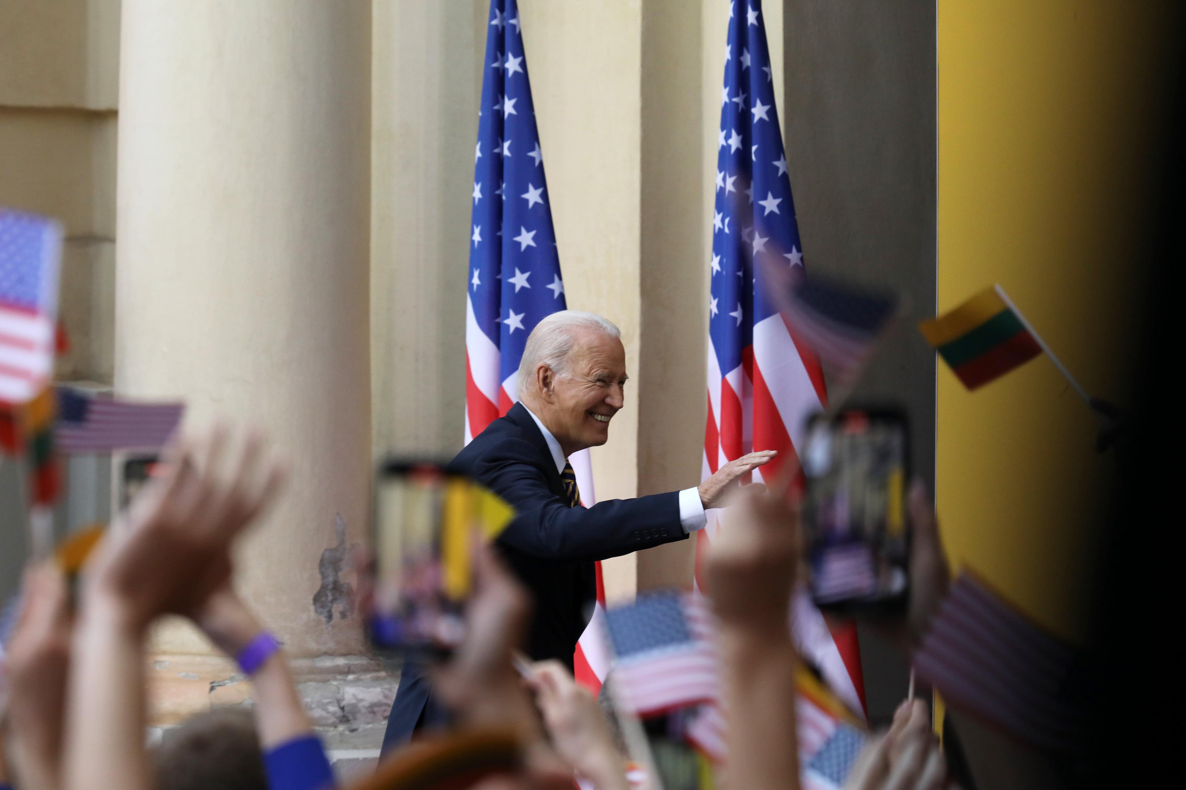 prezydent Joe Biden pozdrawia na tle amerykańskich flag