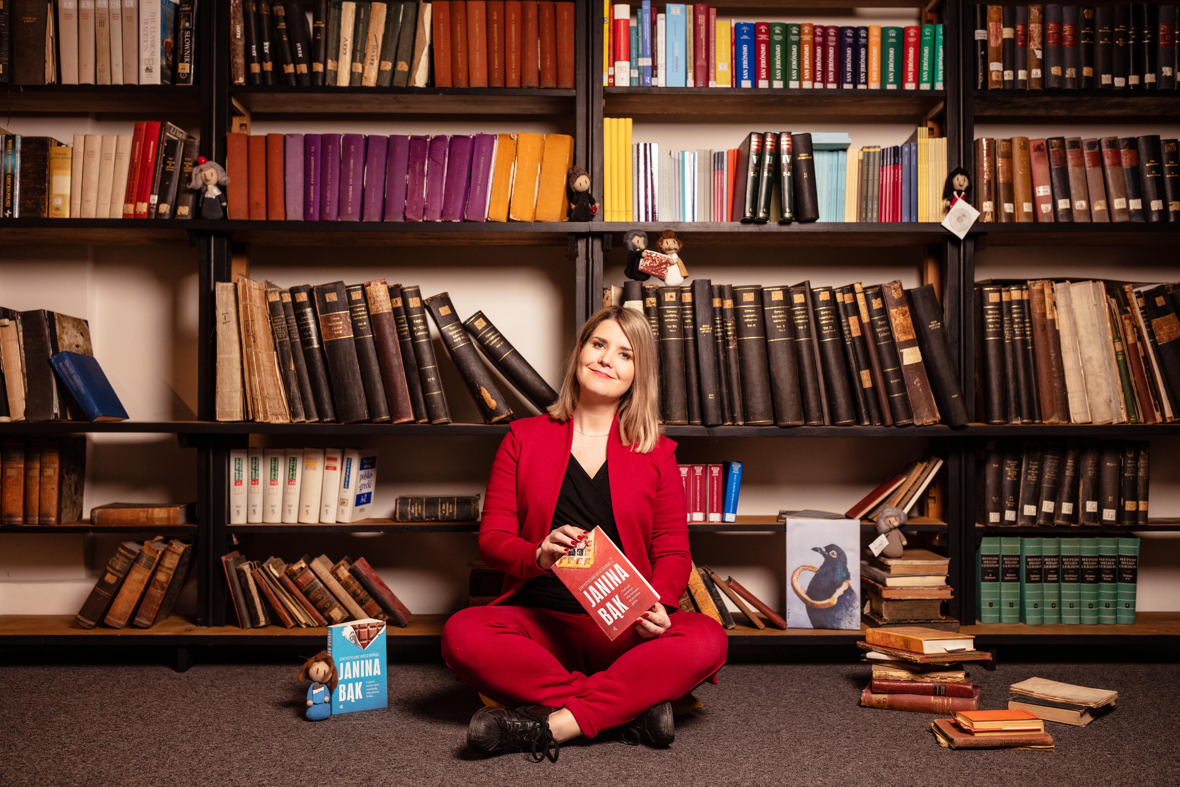 młoda kobieta w czerwonym garniturze na tle półki z książkami