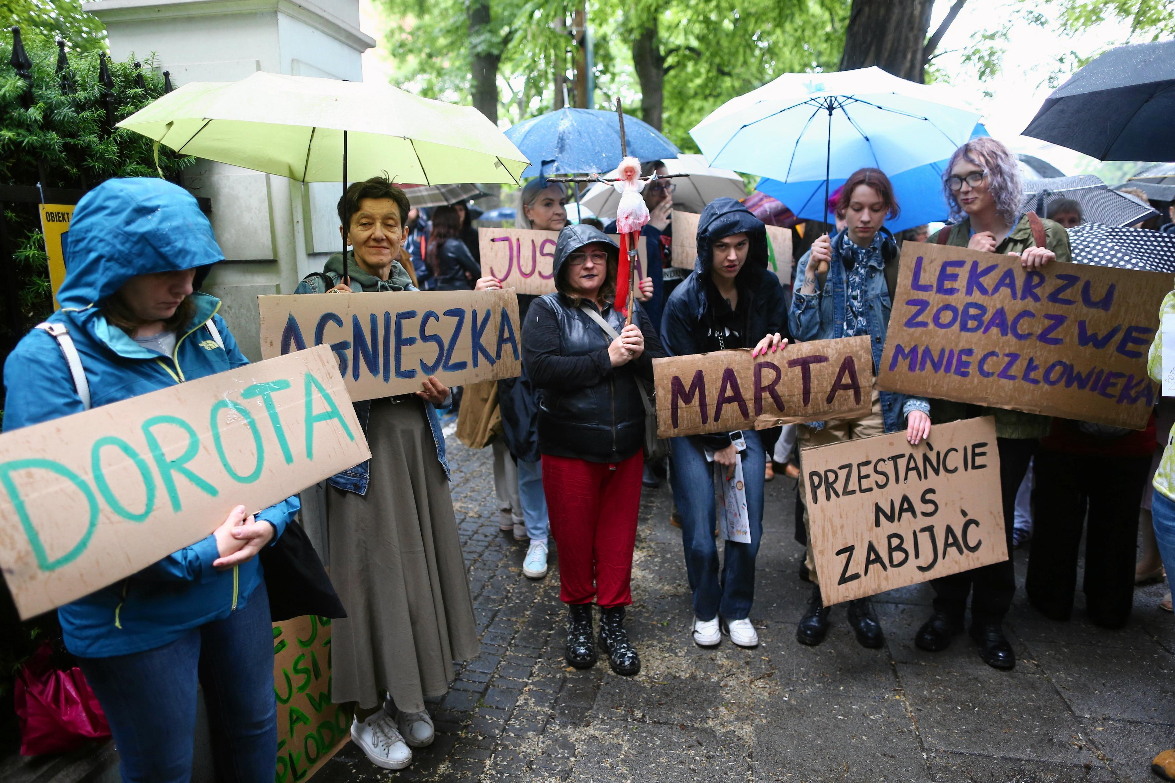 Kilka kobiet protestuje pod parasolkami, na trzymanych transparentach kobiece imiona