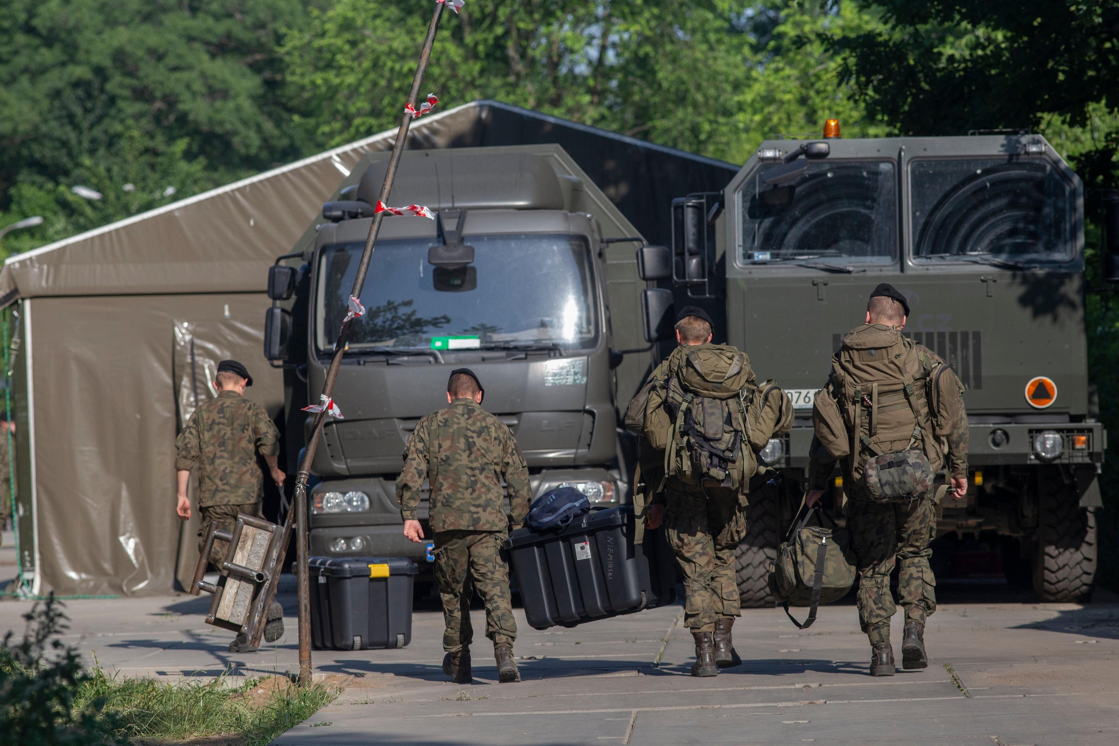 Żołnierze w mundurach idący do wojskowych ciężarówek w Białowieży (zdjęcie od tyłu)