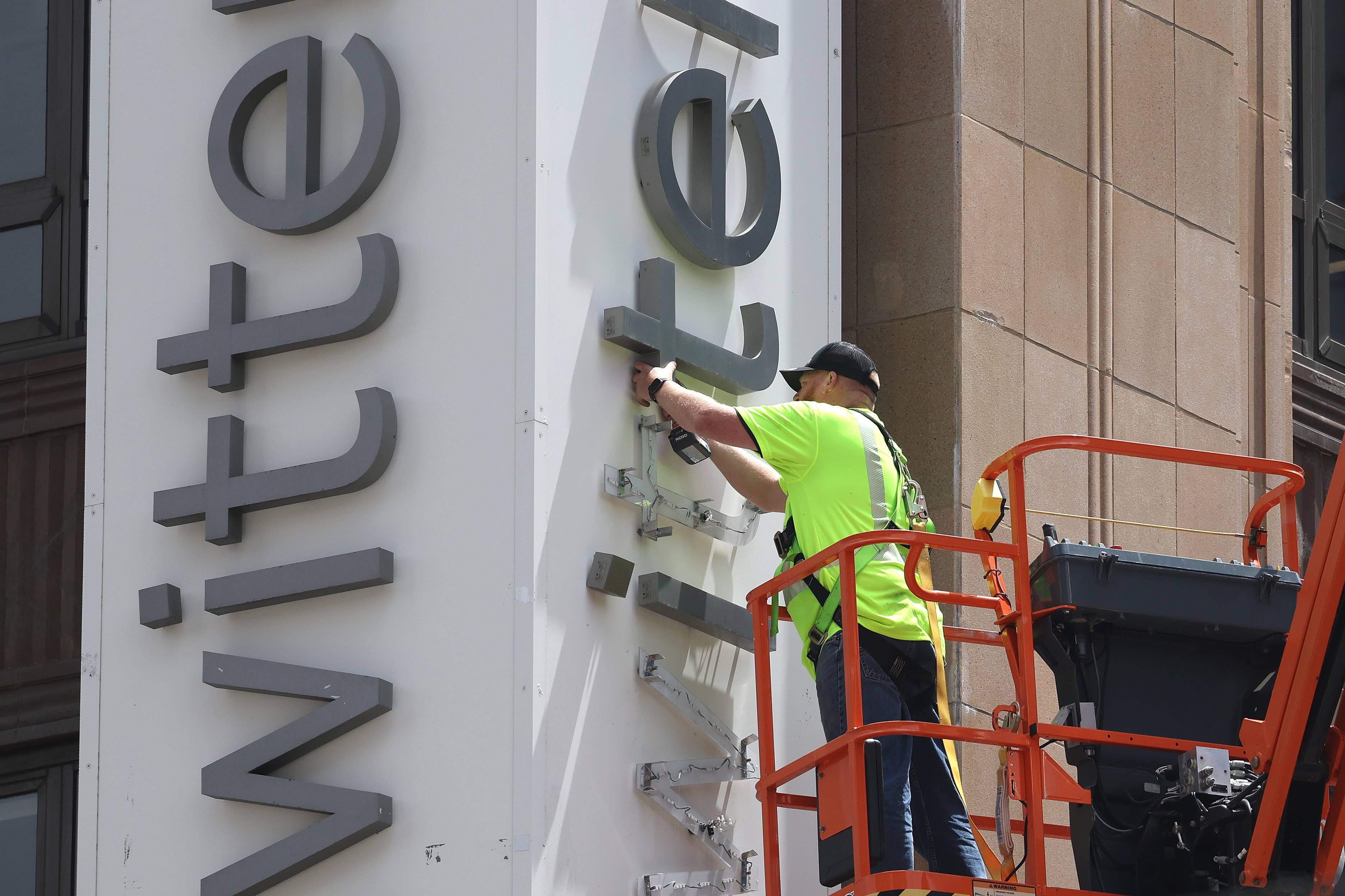 Robotnik stojący na podnośniku demontuje napis Twitter na fasadzie budynku.