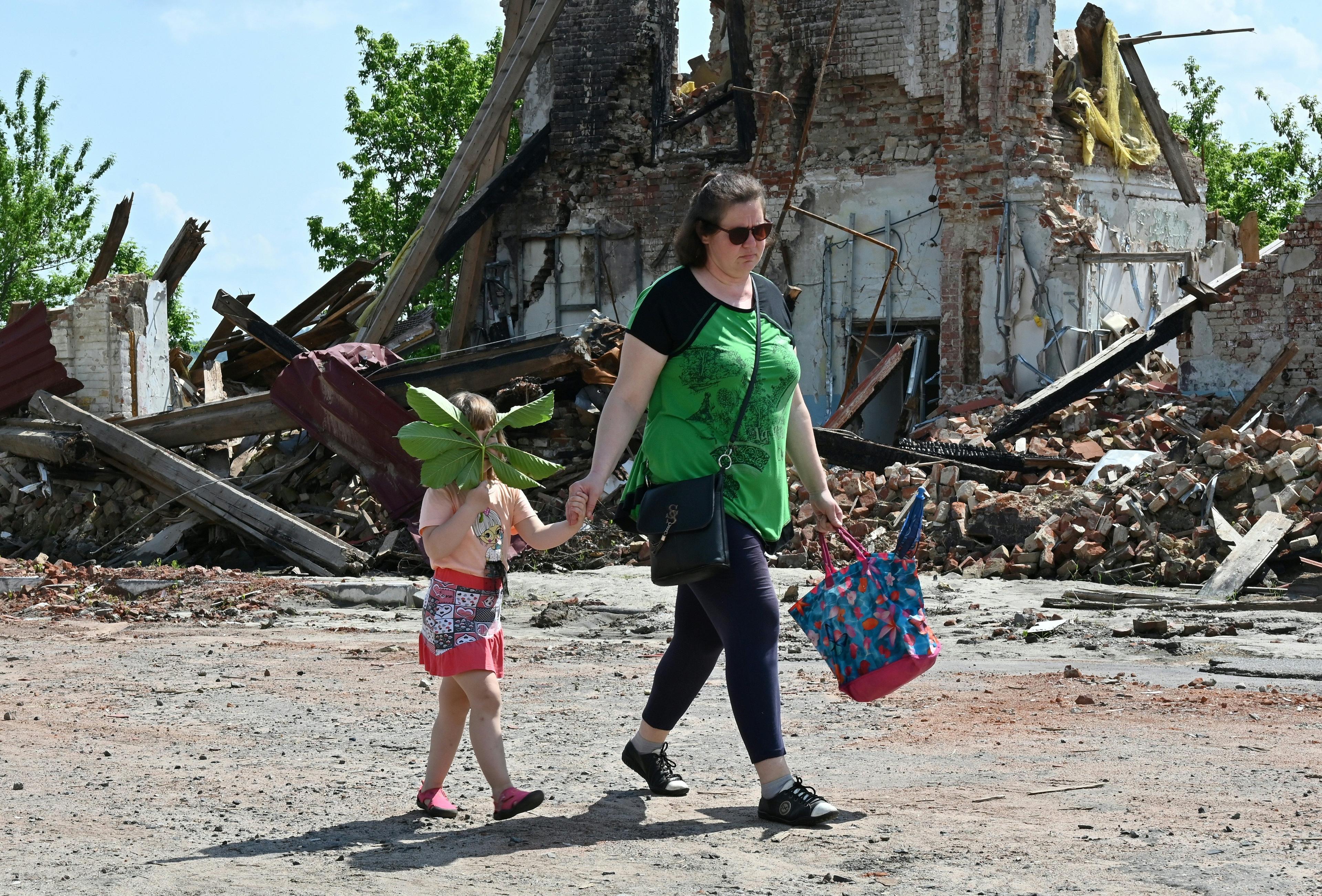 Kobieta z dzieckiem idzie przez zburzone miasto. Dziecko trzyma zielony liść