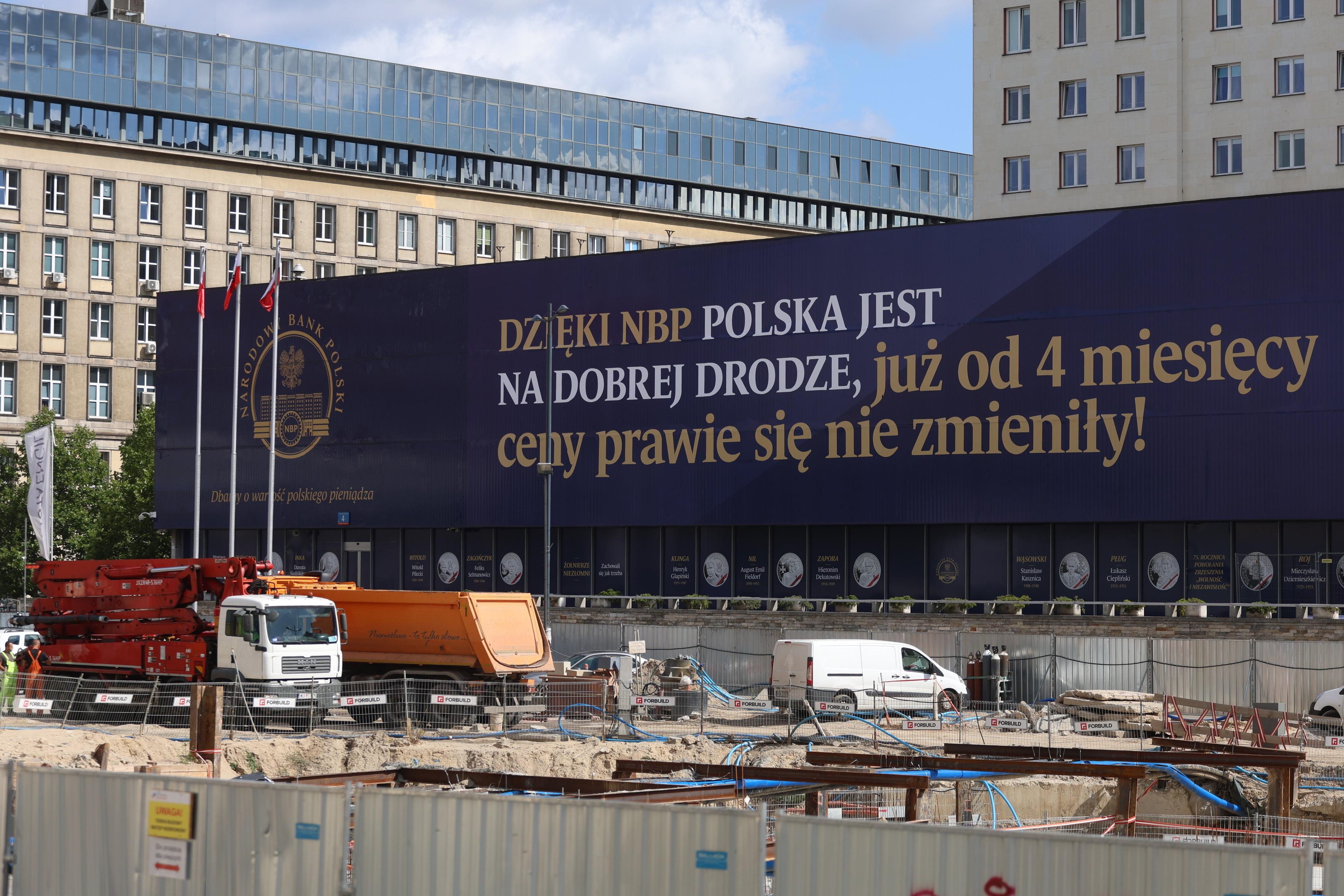 Niebieski baner na budynku z napisem "Dzięki NBP Polska jest na dobrej drodze, już od 4 miesięcy ceny prawie się nie zmieniły"