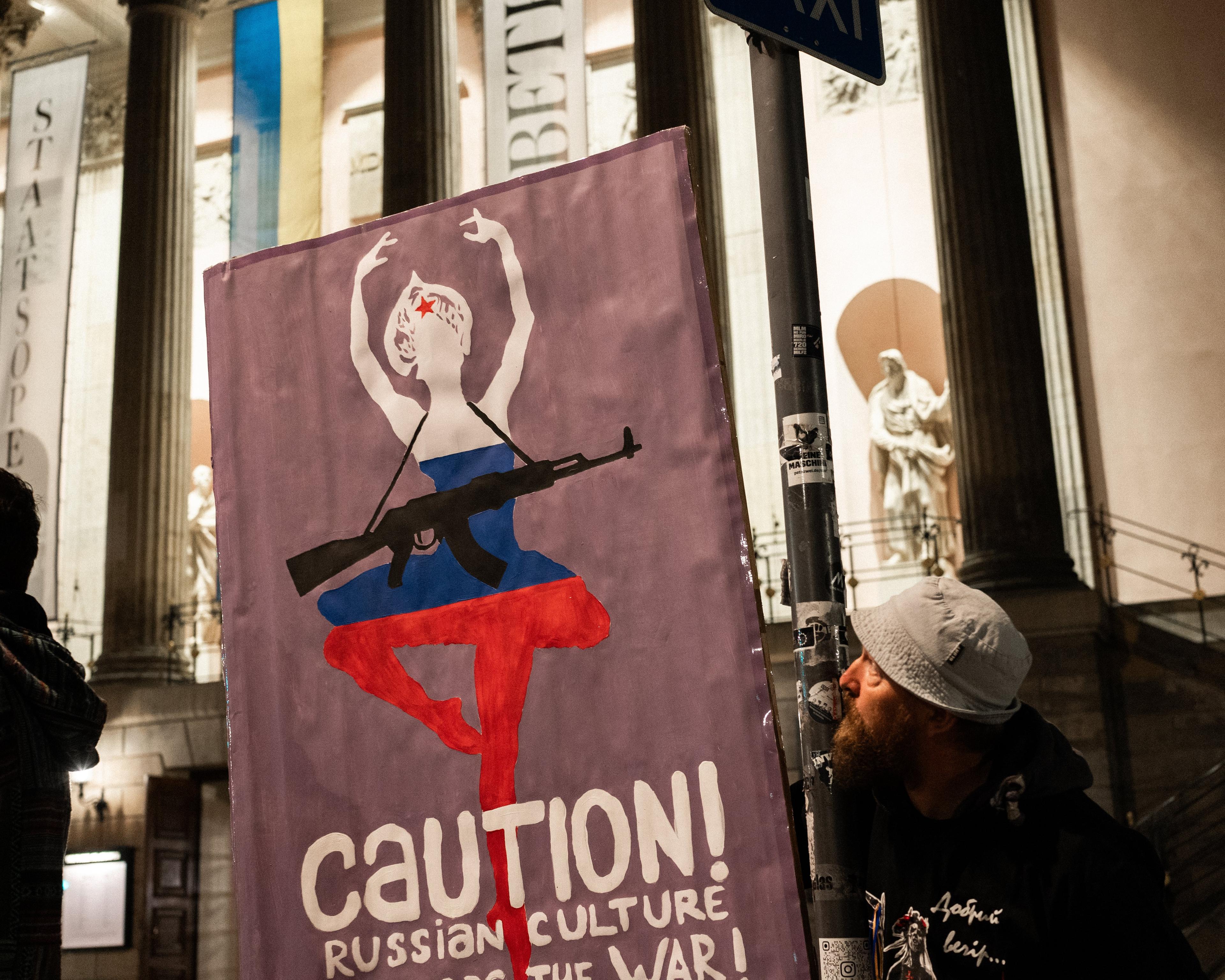 plakat trzymany przez demonstrantów z tancerką z kałasznikowem