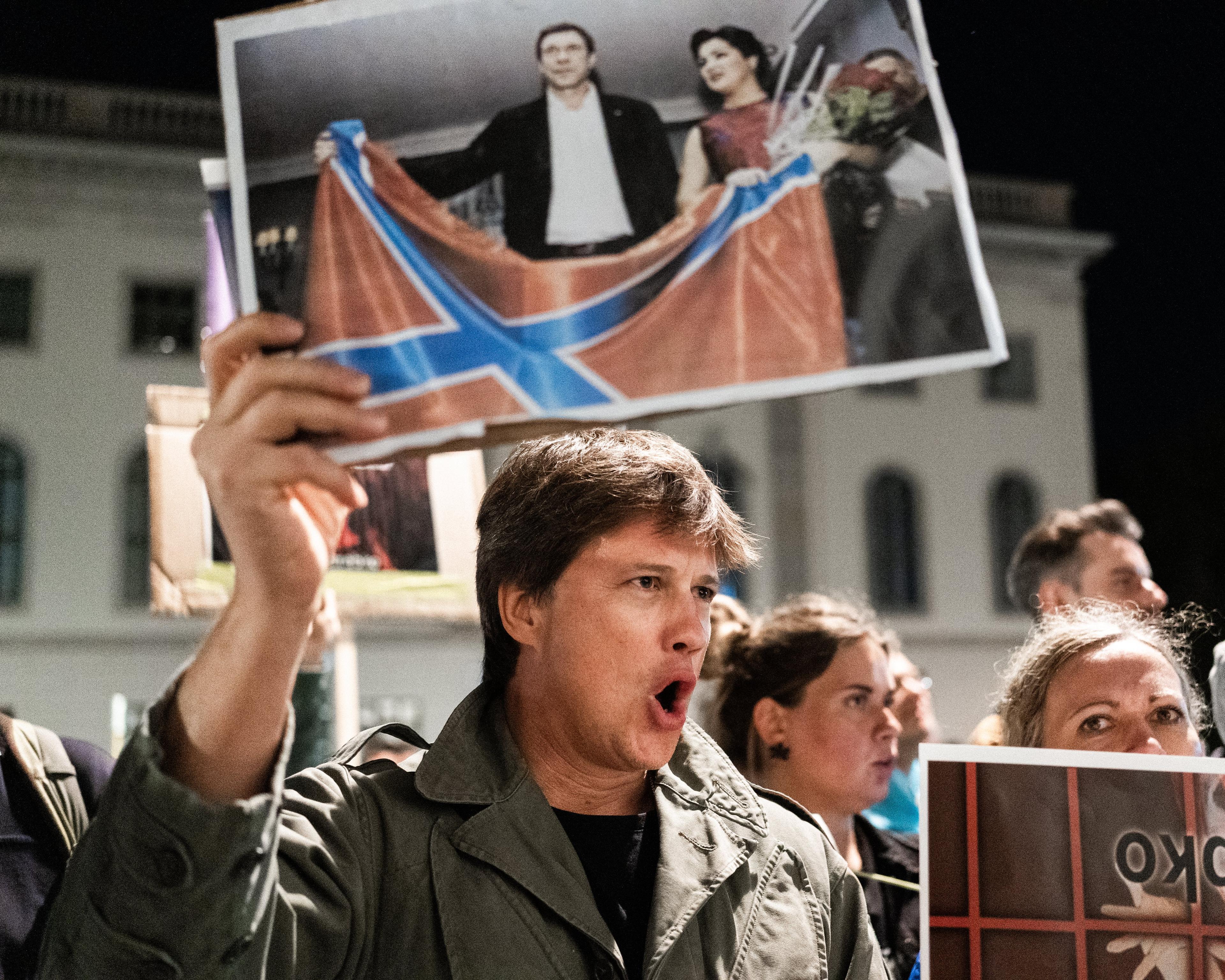 uczestnik protestu ulicznego pokazuje duże zdjęcie z kobietą i mężczyzną trzymającymi flagę rosyjską
