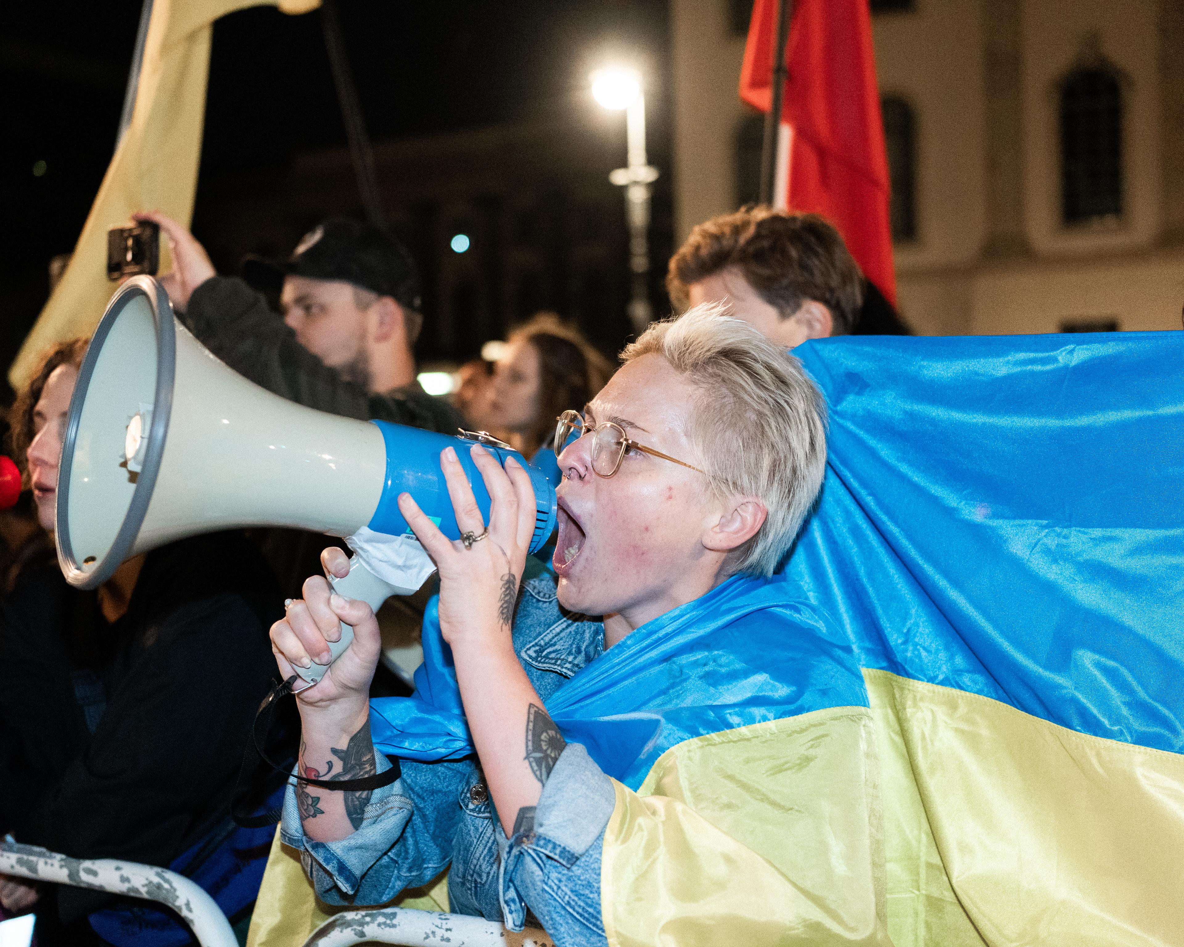 Kobieta krzyczy przez megafon osłonięta flagą Ukraiuny