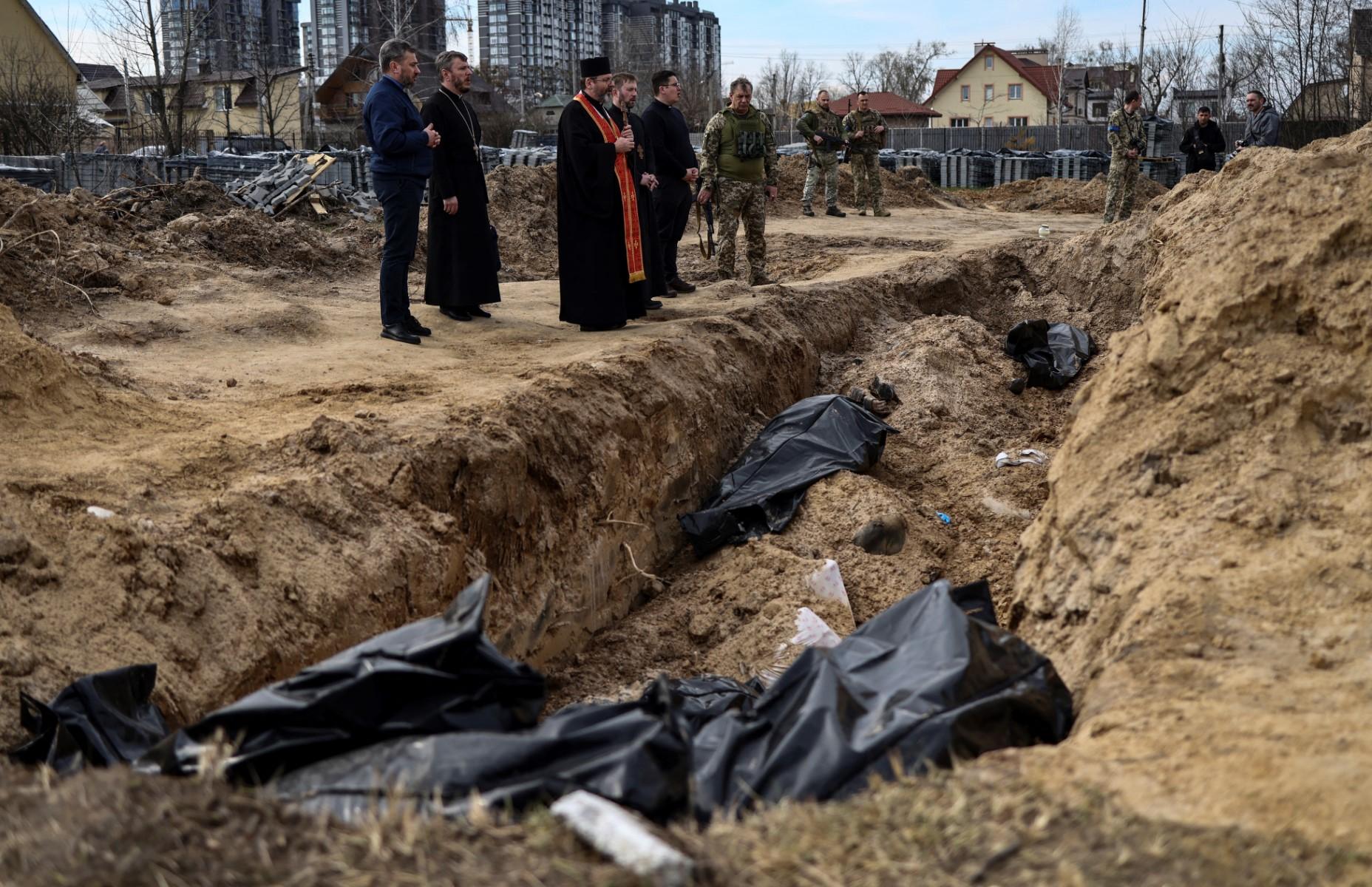 duchowni i żołnierze modlą się nad zbiorową mogiłą, w której leżą worki z ciałami zamordowanych mieszkańców Buczy