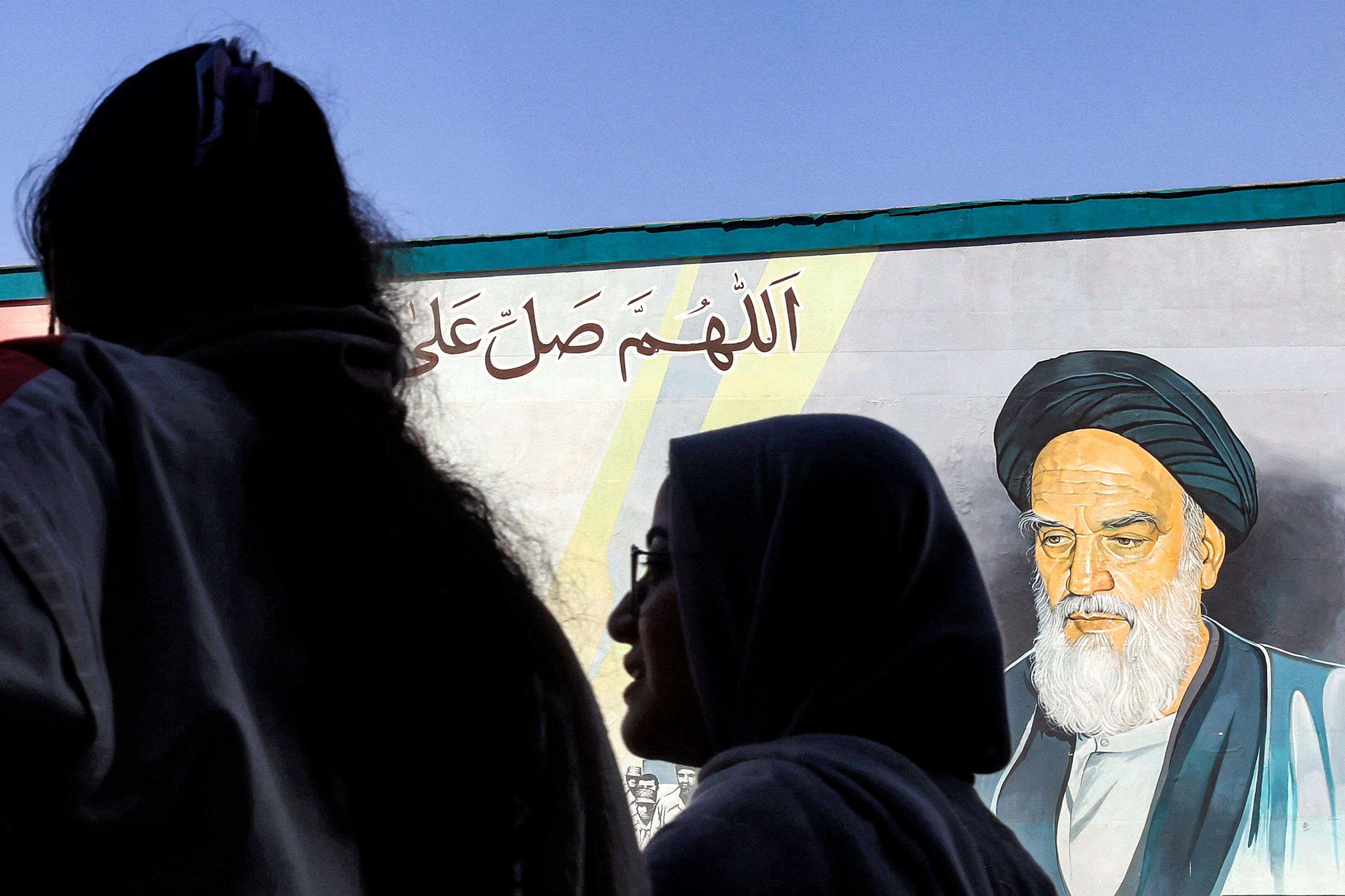 kobiece głowy, jedna w hidżabie, druga bez, w tle mural z Chomeinim