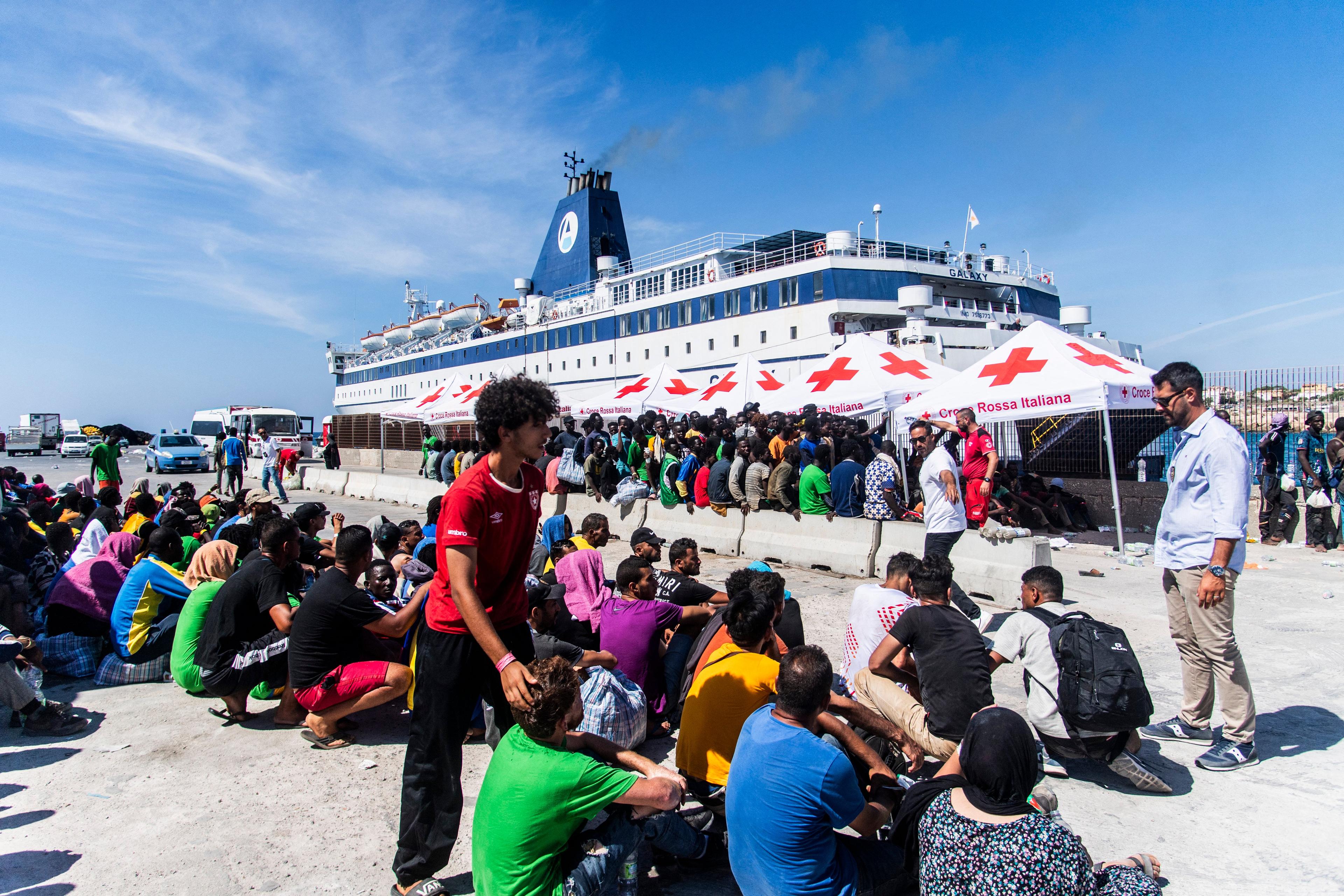 Migranci z ośrodka dla migrantów na włoskiej wyspie Lampedusa są oprowadzani przez pracownika ochrony 14 września 2023 r., gdy przygotowują się do wejścia na pokład statku "Galaxy" płynącego do sycylijskiego miasta Porto Empedocle.