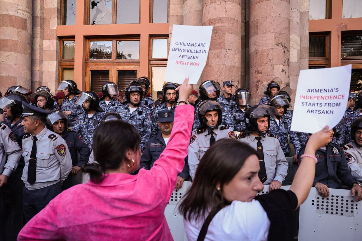 Demonstranci trzymają transparenty, podczas gdy ormiańscy funkcjonariusze organów ścigania w strojach bojowych pilnują wejścia do budynku rządowego podczas wiecu w Erywaniu 21 września 2023 r., po azerbejdżańskich operacjach wojskowych przeciwko siłom ormiańskich separatystów w Górskim Karabachu.