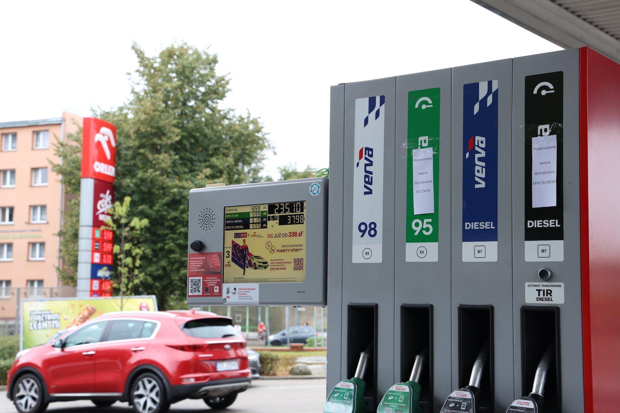 Zdjęcie nieczynnego dystrybutora na stacji Orlen. W tle wyjeżdżające ze stacji czerwone auto.