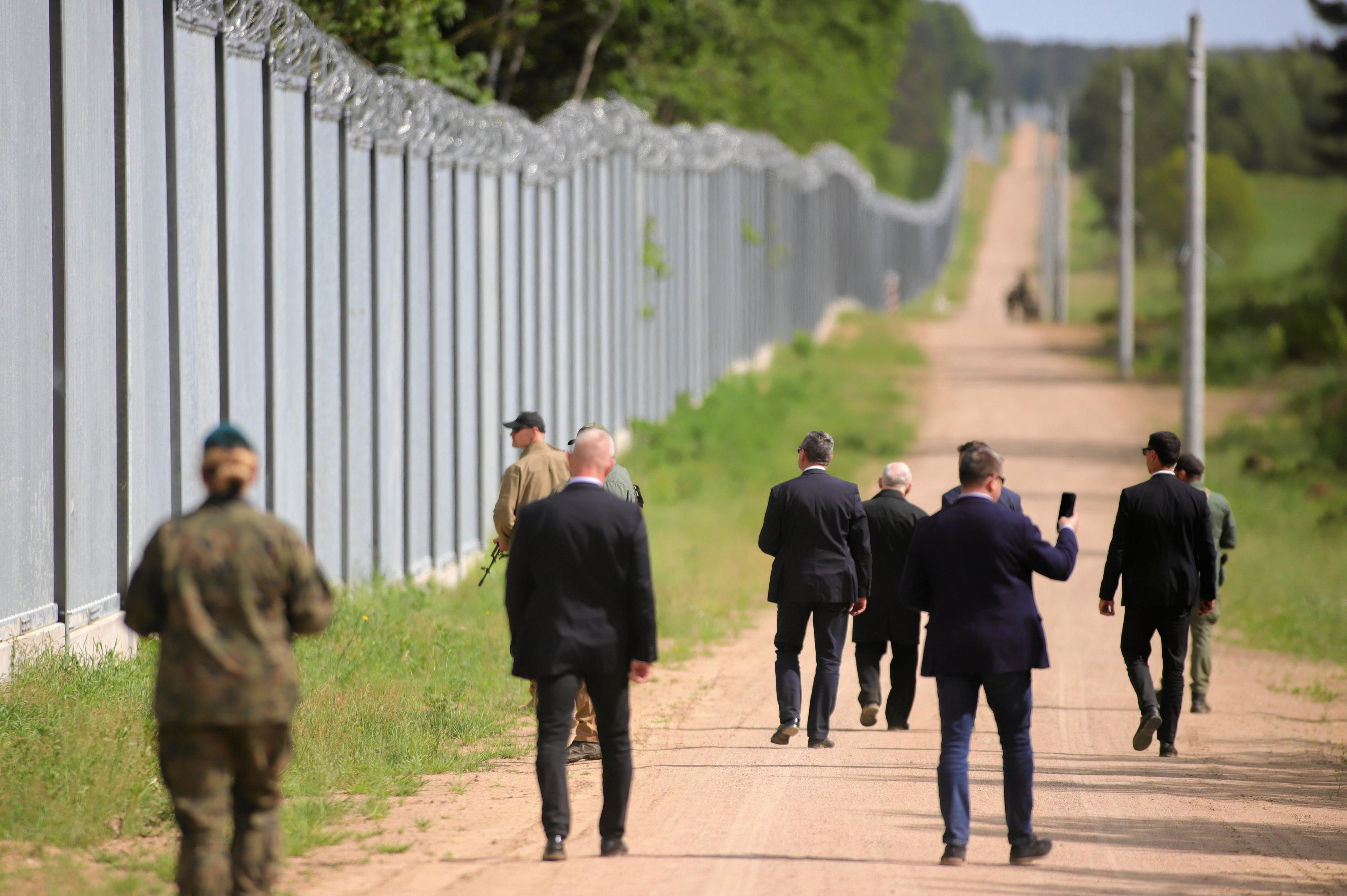 Jarosław Kaczyński w otoczeniu ochroniarzy idzie wzdłuż płotu na granicy białoruskiej (zdjęcie od tyłu)