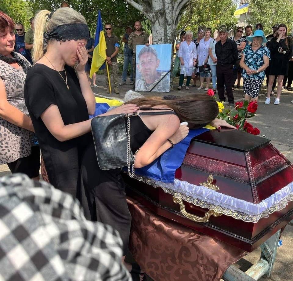 pogrzeb ukraińskiego zołnierza, kobieta przytula się do drewnianej trumny, druga kobieta zasłania twarz