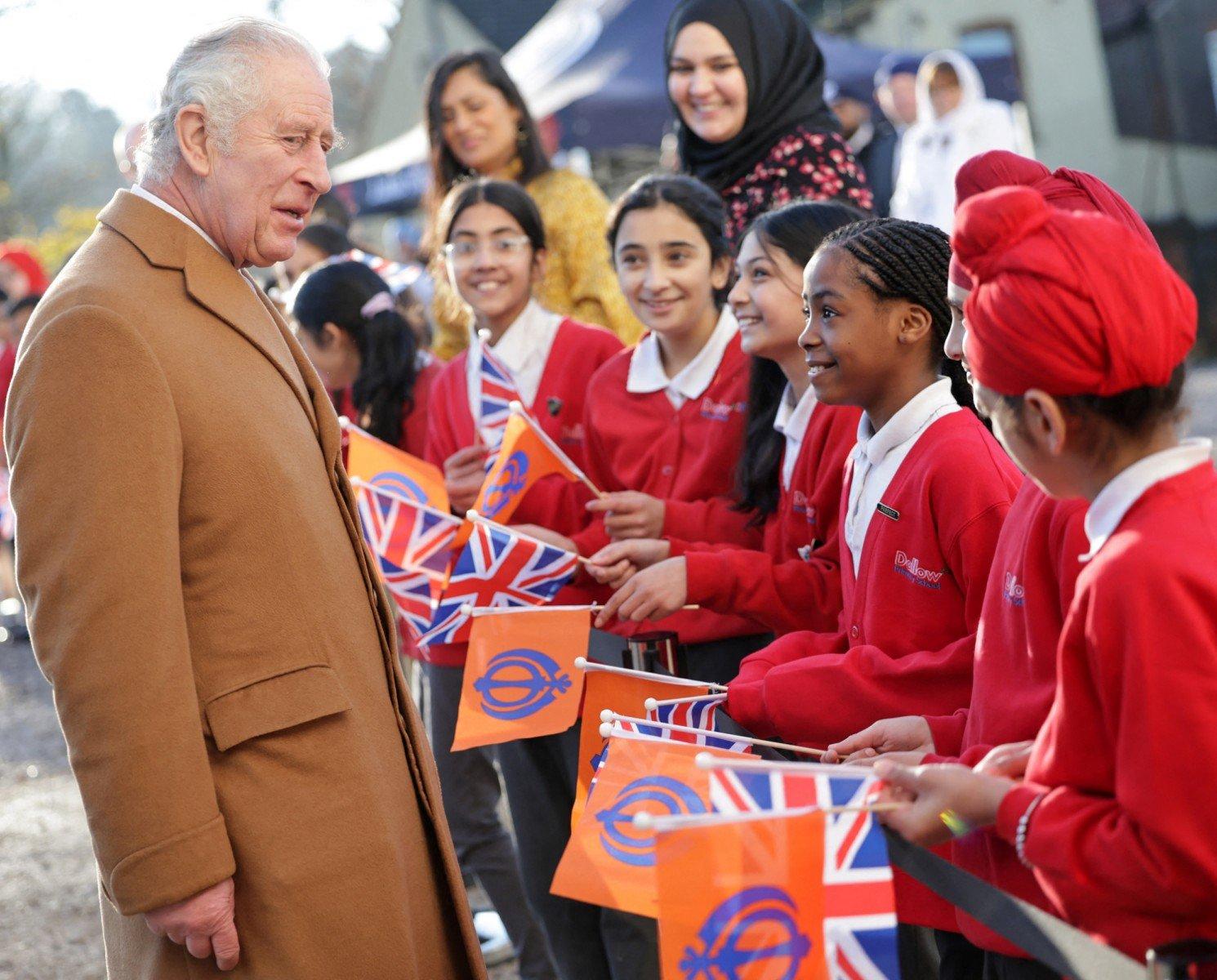 Król Karol rozmawia z dziećmi z różnych narodowości, trzymających flagi brytyjskie
