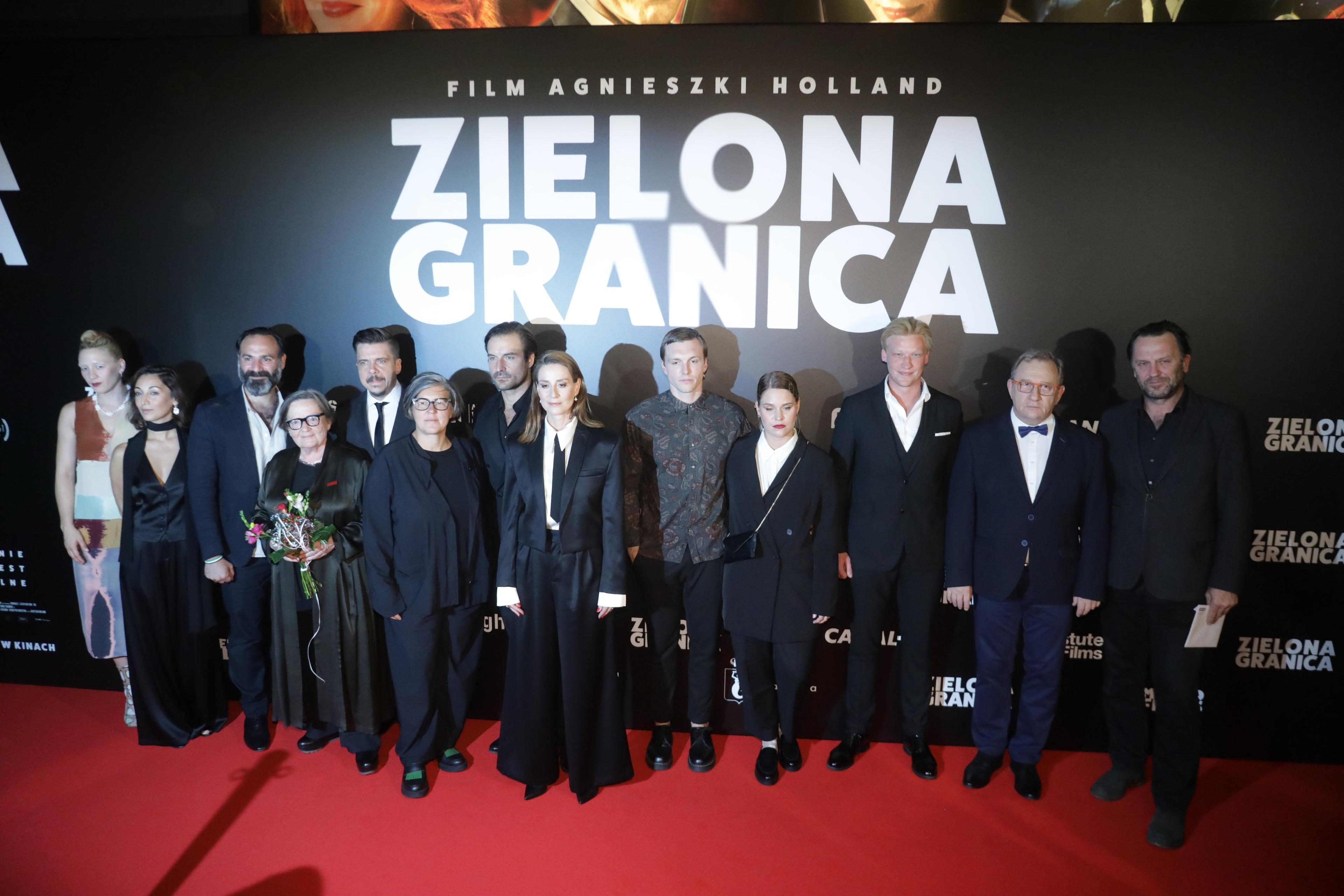 Agnieszka Holland wraz z ekipą filmową stoi na czerwonym dywanie, za nimi na czarnym tle duży napis "Zielona granica"