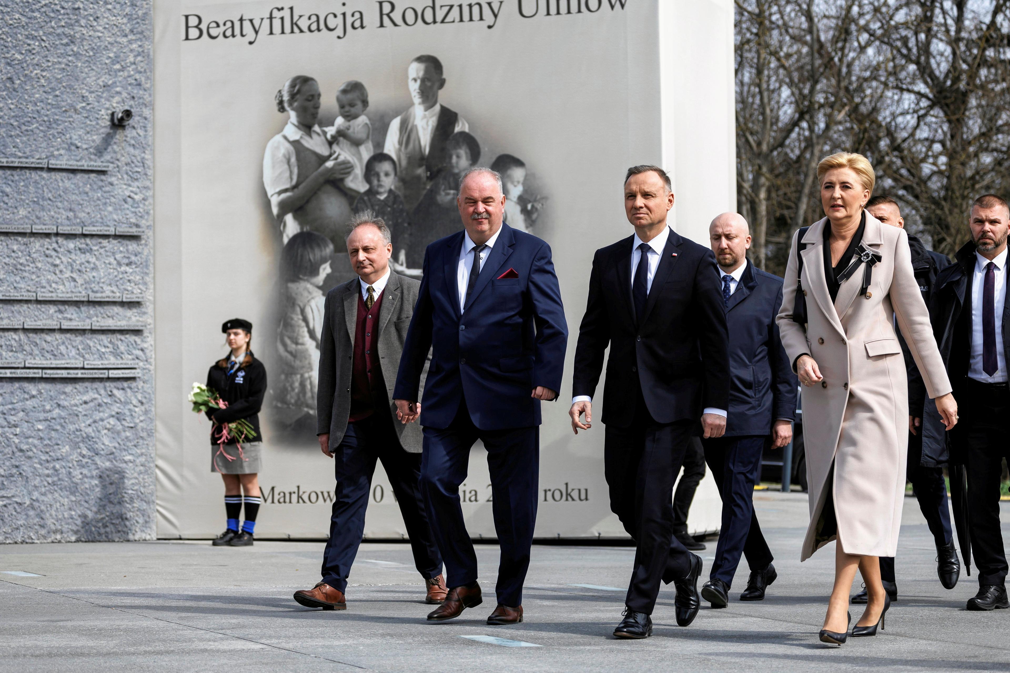 Prezydent Andrzej Duda z małżonką i urzędnikami idzie dziedzińcem muzeum, w tle platak przedstawiający zdjęcie rodziny z dziećmi z napisem Beatyfikacja Rodziny Ulmów