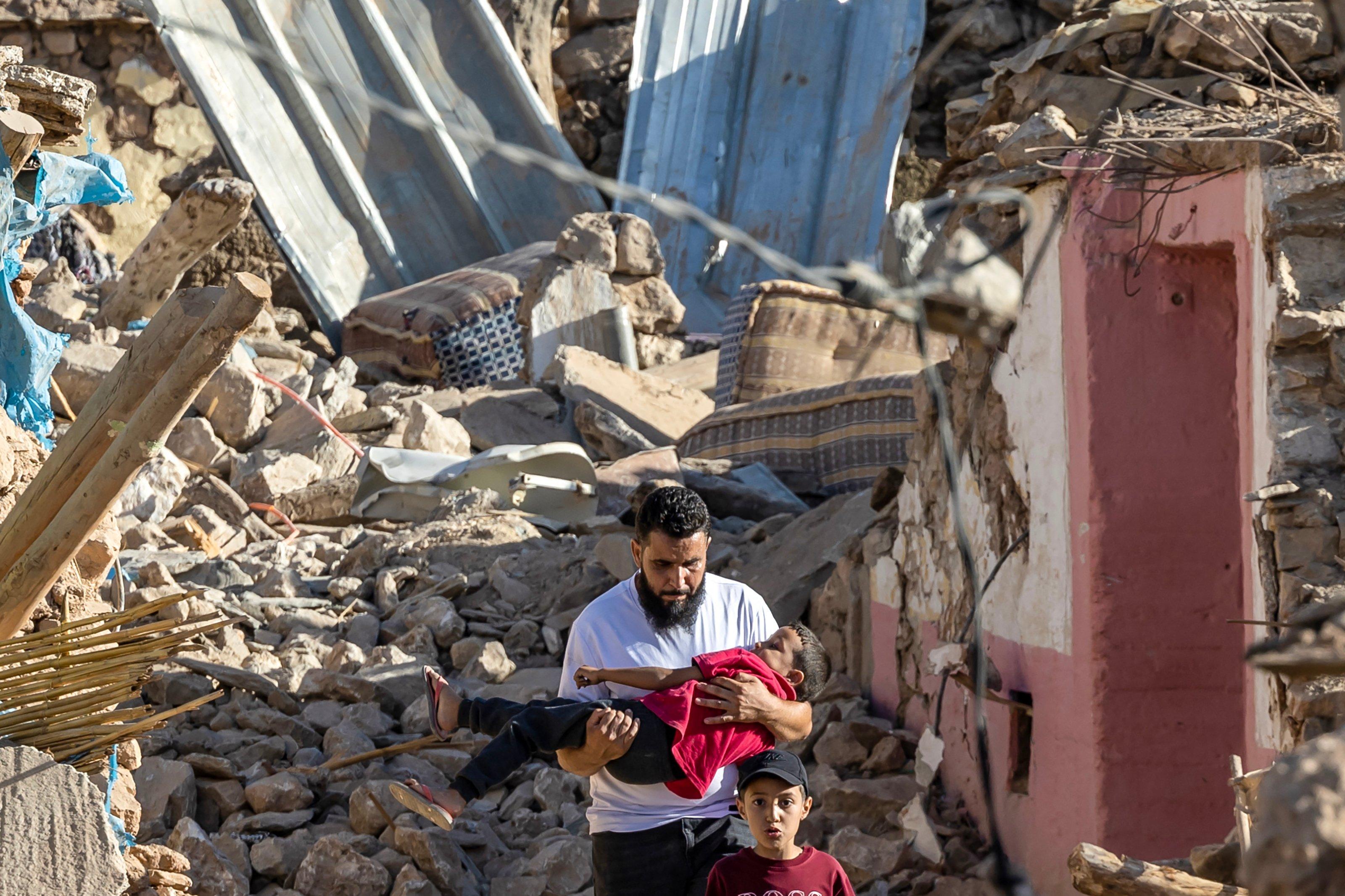 A man carries a boy as he walks past destroyed houses after an earthquake in the mountain village of Tafeghaghte, southwest of Marrakesh, on September 9, 2023. - Moroccans on September 10 mourned the victims of a devastating earthquake that killed more than 2,000 people, as rescue teams raced to find survivors trapped in the rubble of flattened villages. (Photo by Fadel SENNA / AFP)