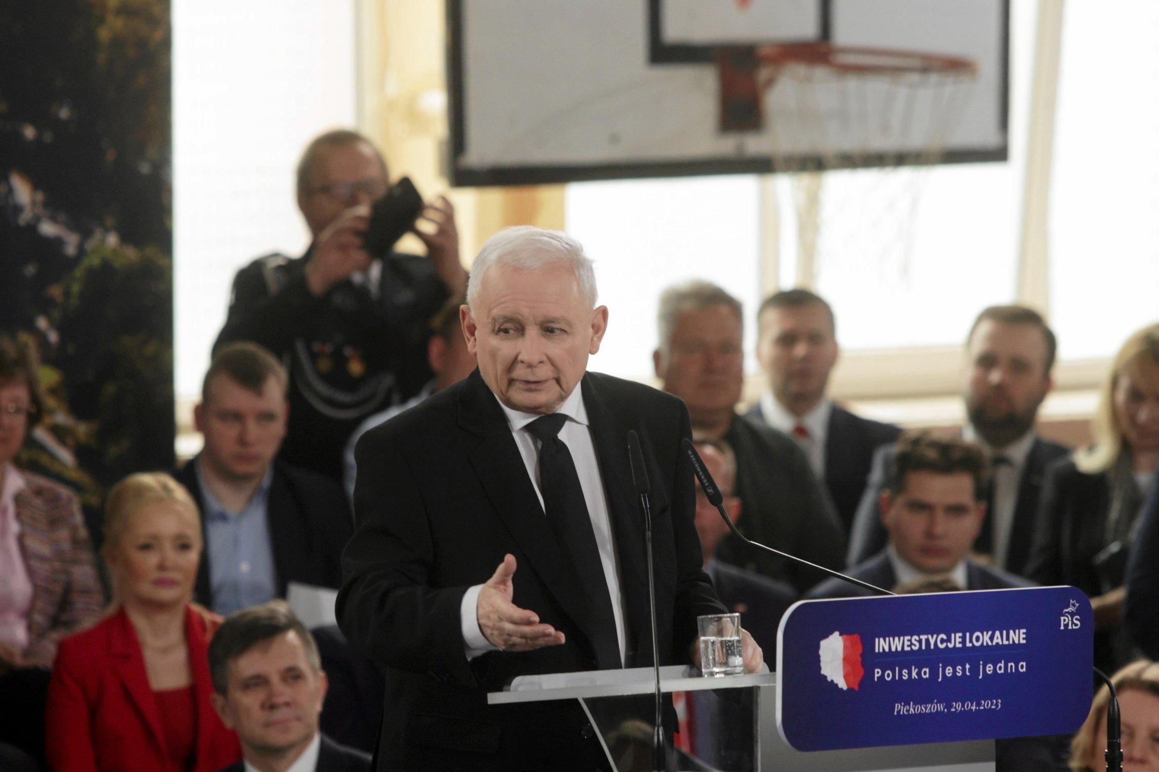 Jarosław Kaczyński w garniturze na sali gimnastycznej. Za nim kosz i tablica do koszykówki