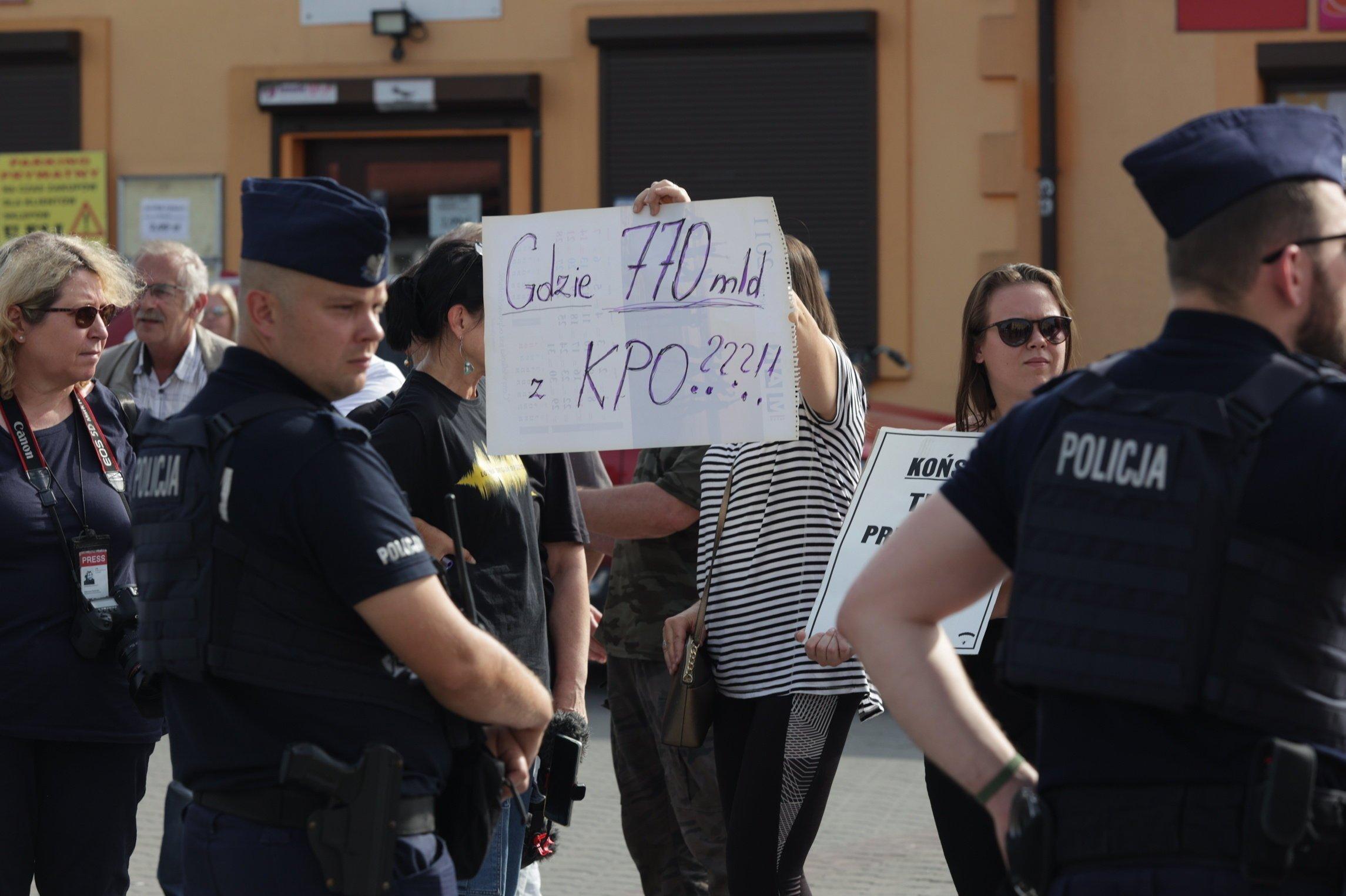 Kobieta z plakatem "Gdzie 770 mld z KPO" i policjanci