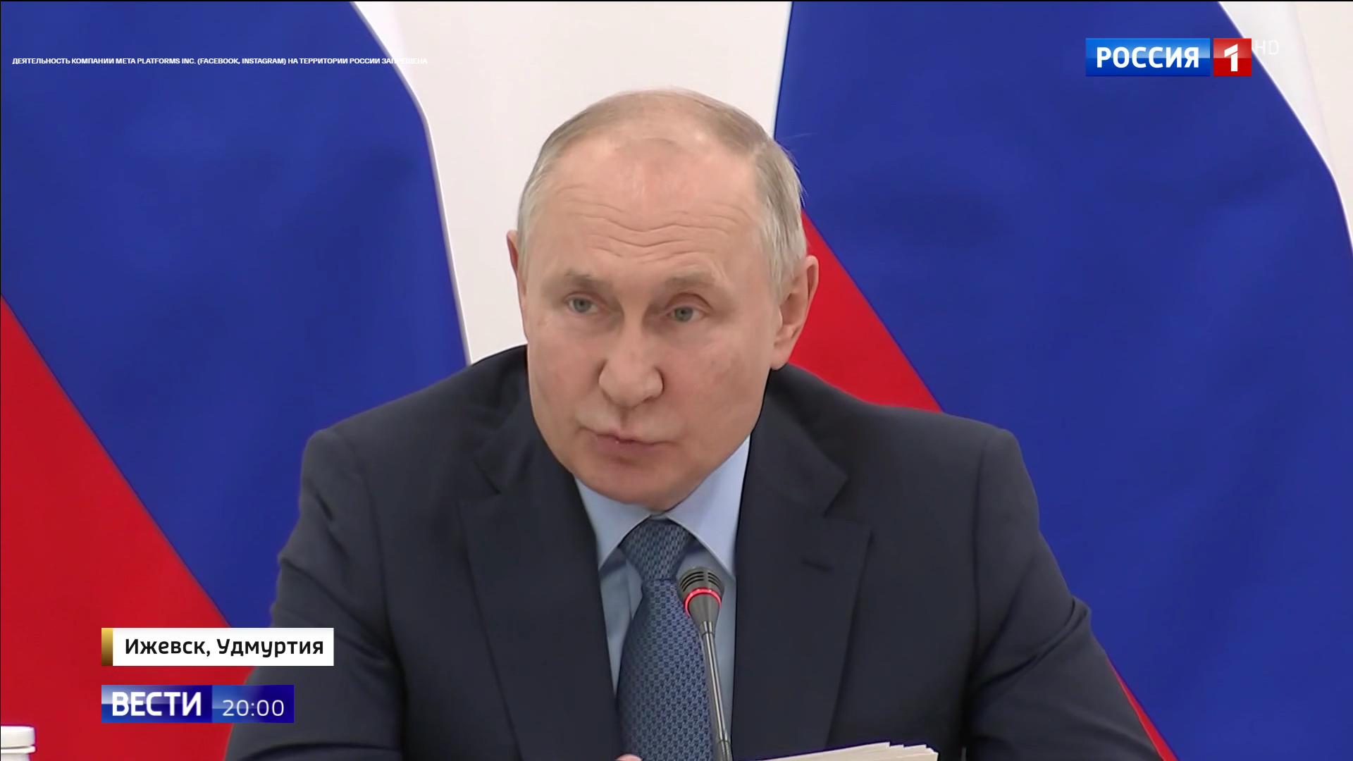 Putin siedzi i mówi na tle rosyjskiej flagi.