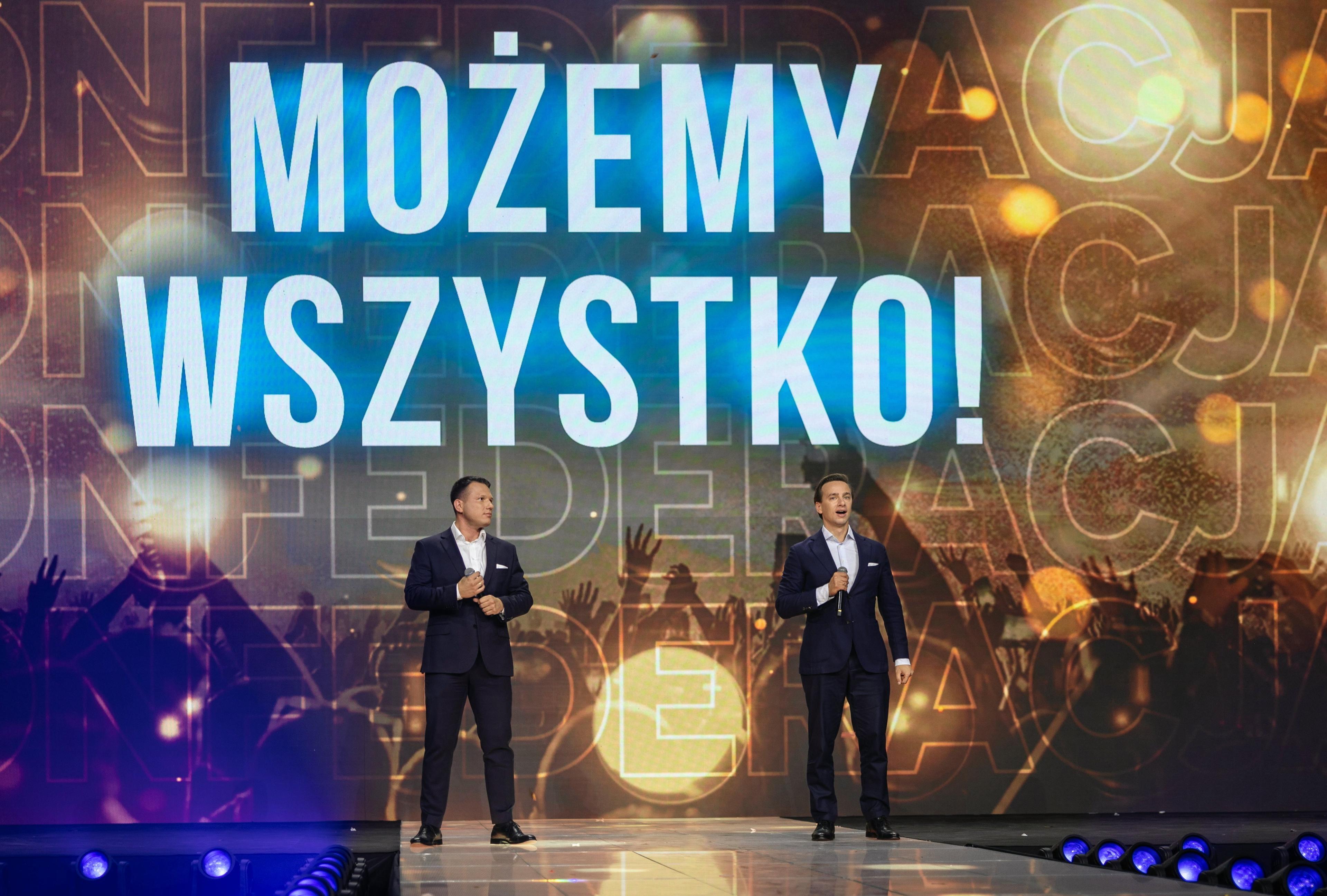 Sławomir Mentzen i Krzysztof Bosak z Konfederacji stoją na dużej scenie, w tle żółte kolory scenografii i jasno-niebieski duży napis: Możemy wszystko!